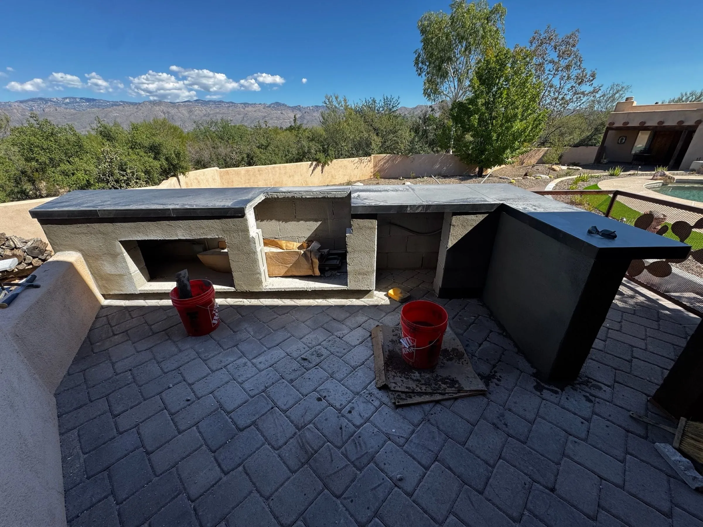 L-shaped outdoor kitchen counter under construction on a paver patio with mountain views.