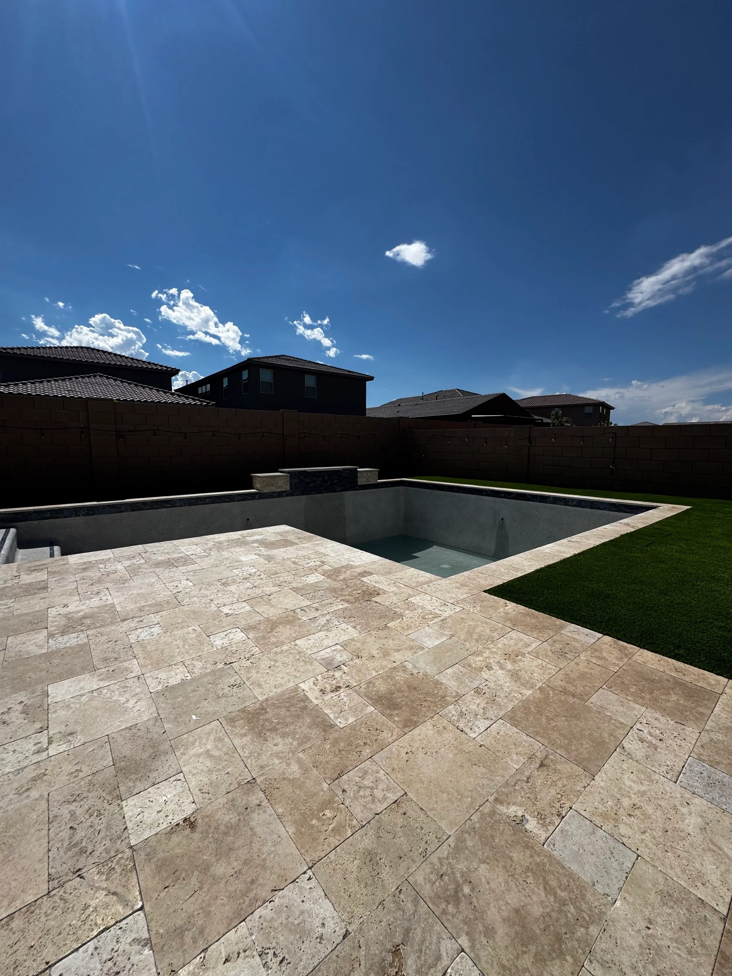 Geometric pool with a travertine deck and turf on a sunny Tucson day, sanitized with low-chlorine water treatment