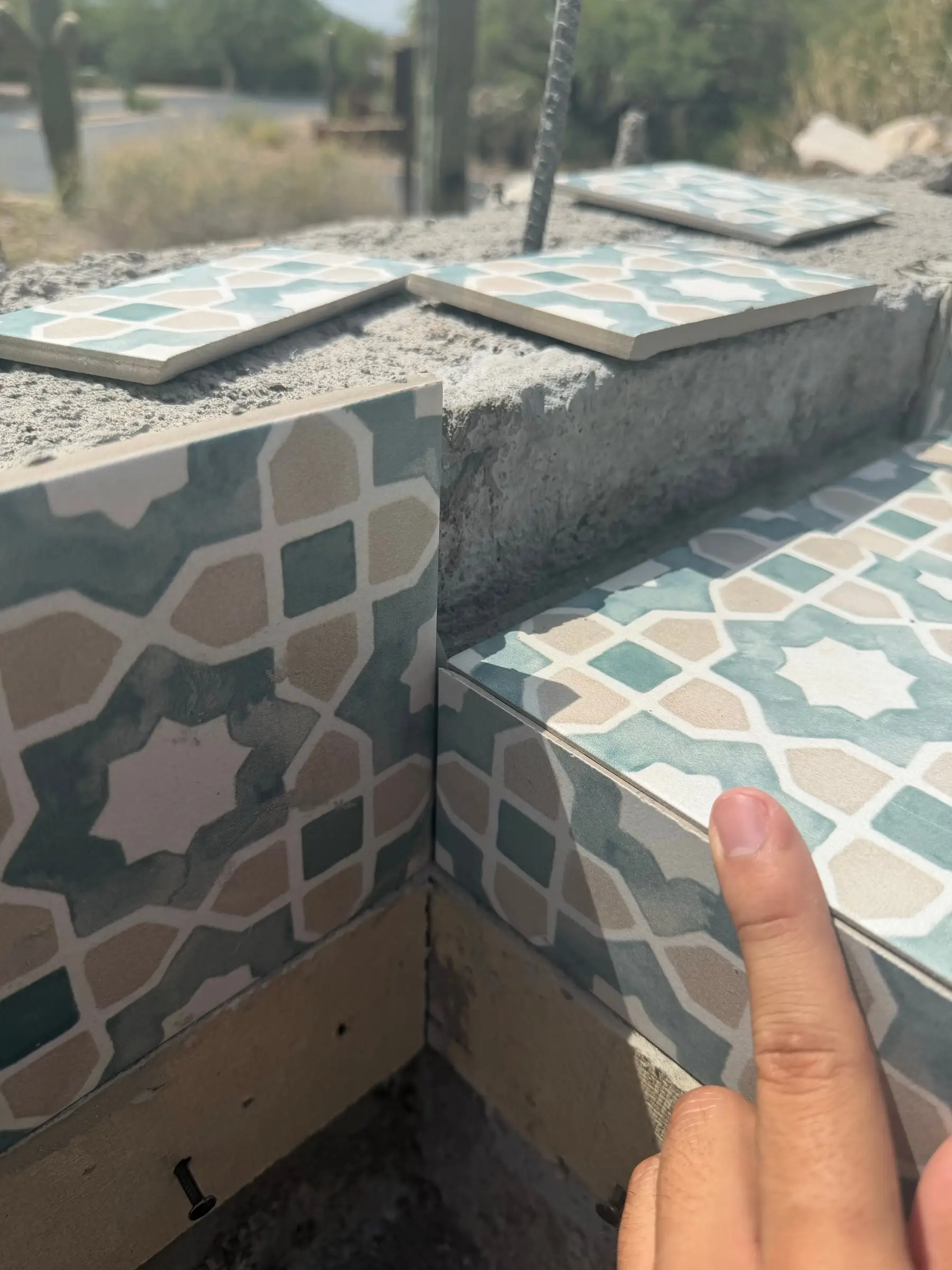 Patterned teal and tan ceramic tile being dry-fit on a raised pool wall