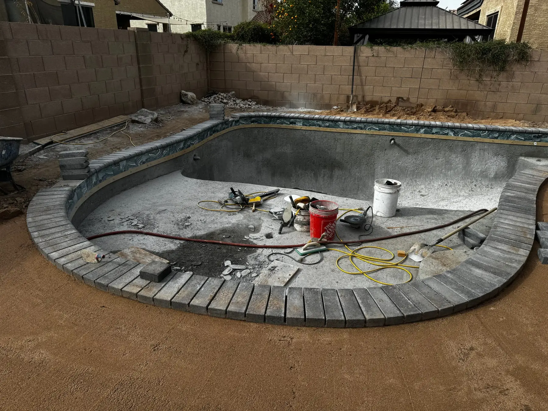 Gray paver coping set around a freeform pool shell before the interior finish.