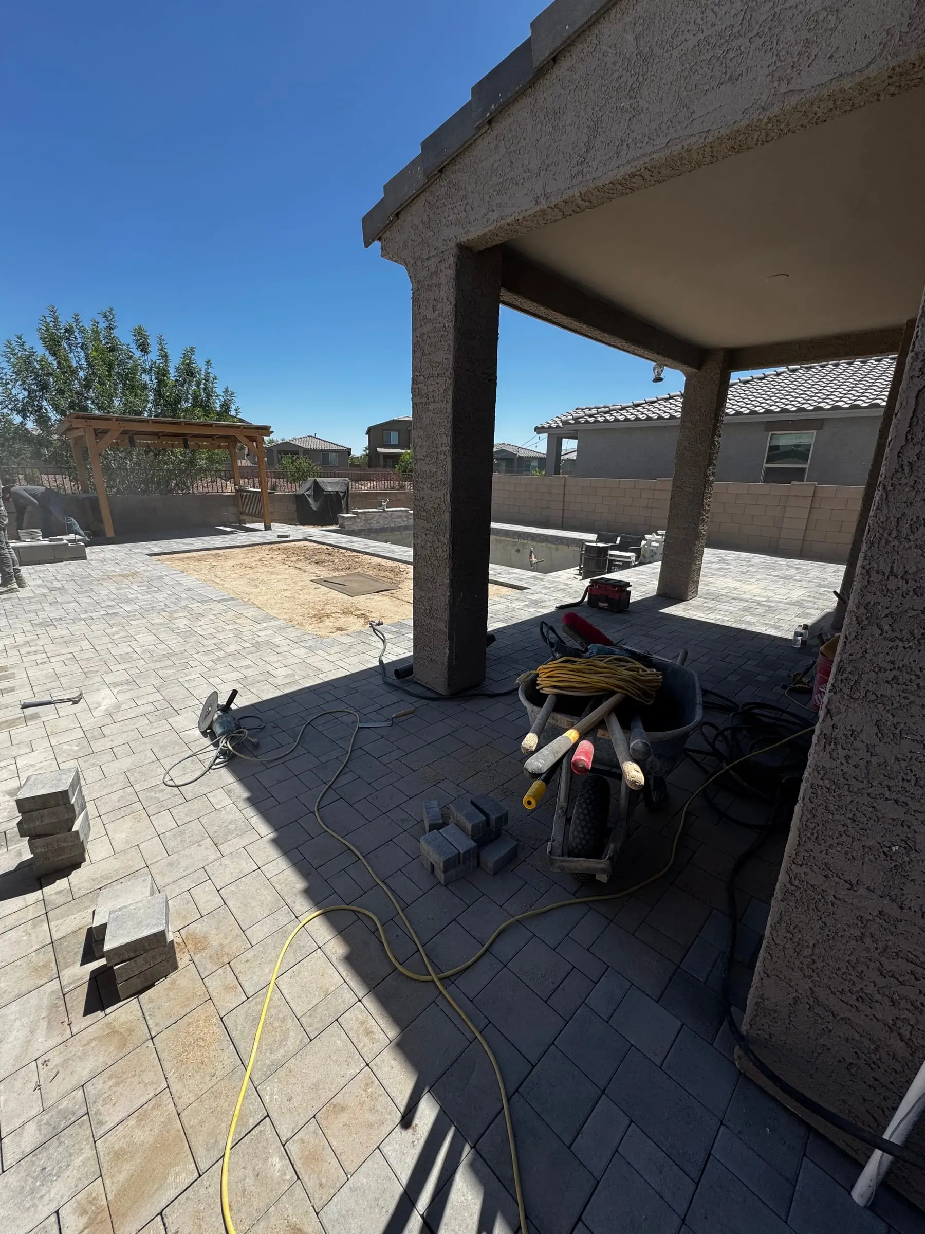 Gray paver deck going in under a covered patio next to a new pool, Marana, AZ.