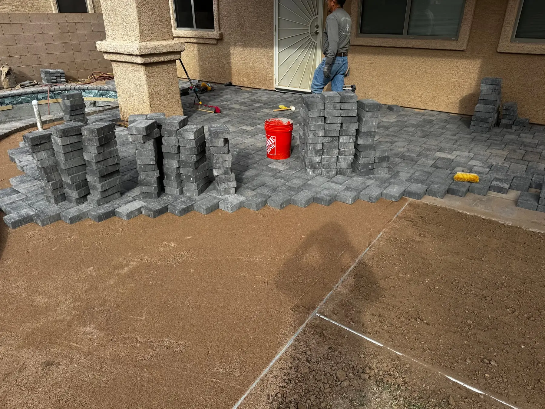Gray pavers stacked and being laid for a new patio beside a pool under construction, Marana, AZ.