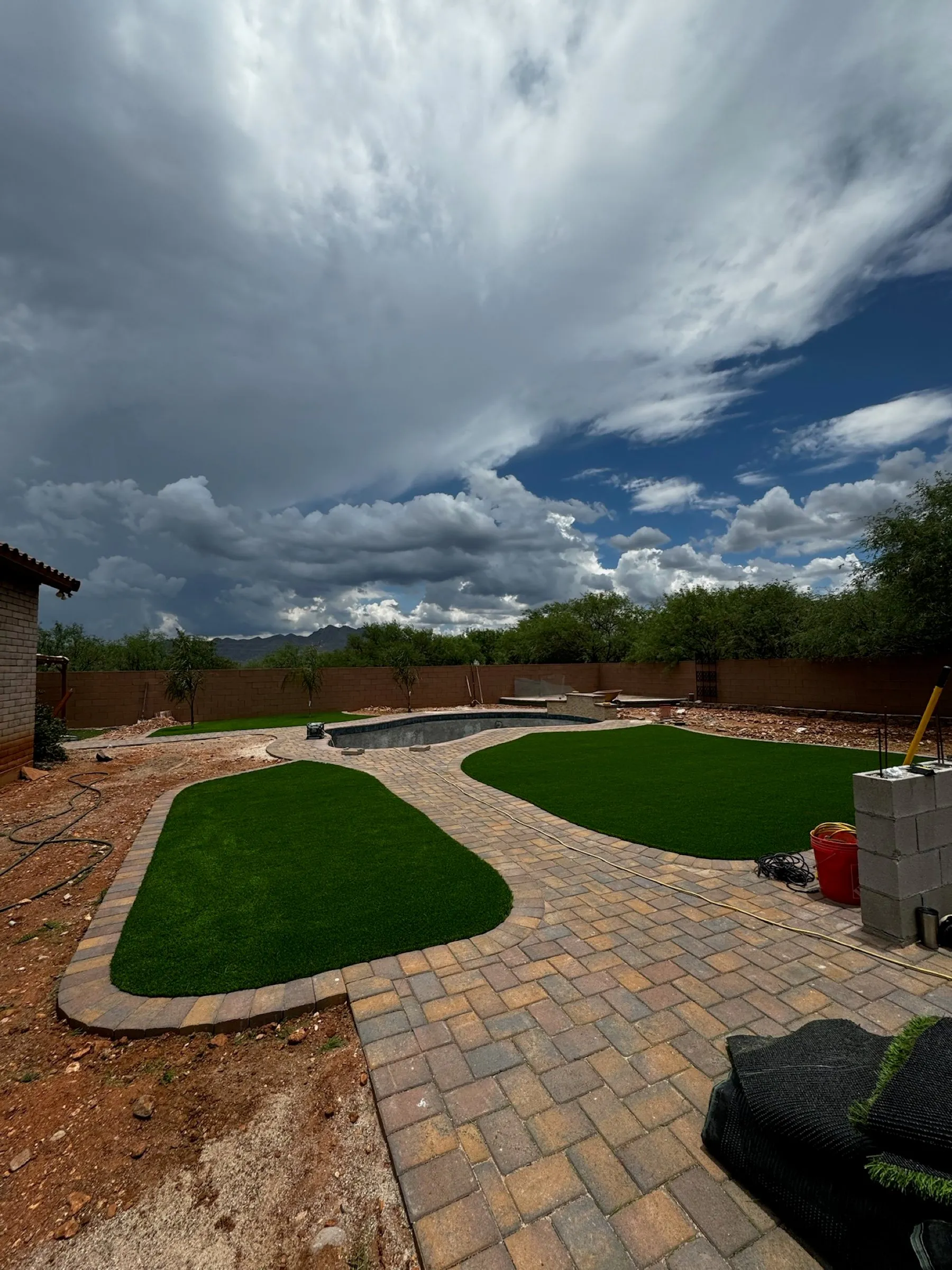 New paver patio with curved artificial turf islands under a monsoon sky in the Tucson area.