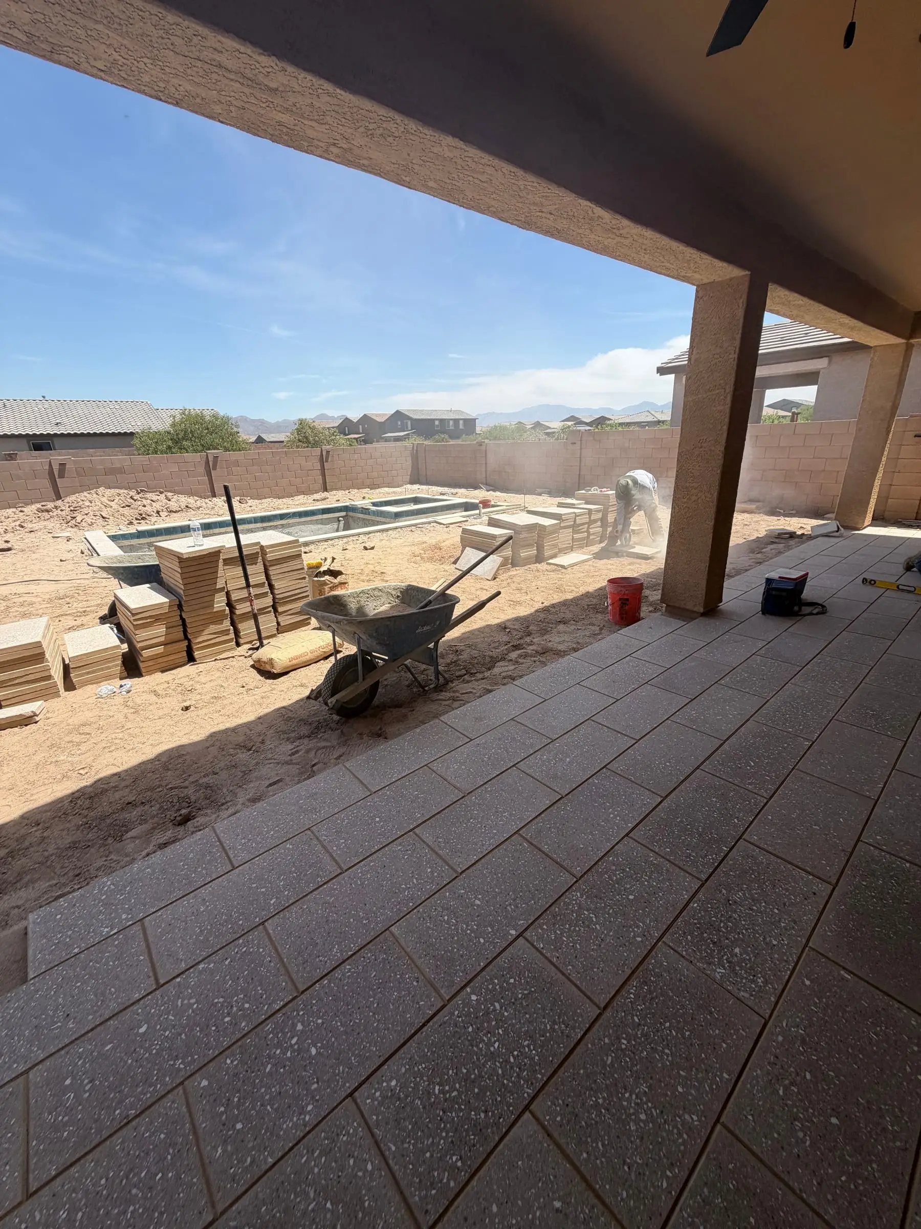 New paver patio under a covered porch, looking out at a pool and spa under construction.