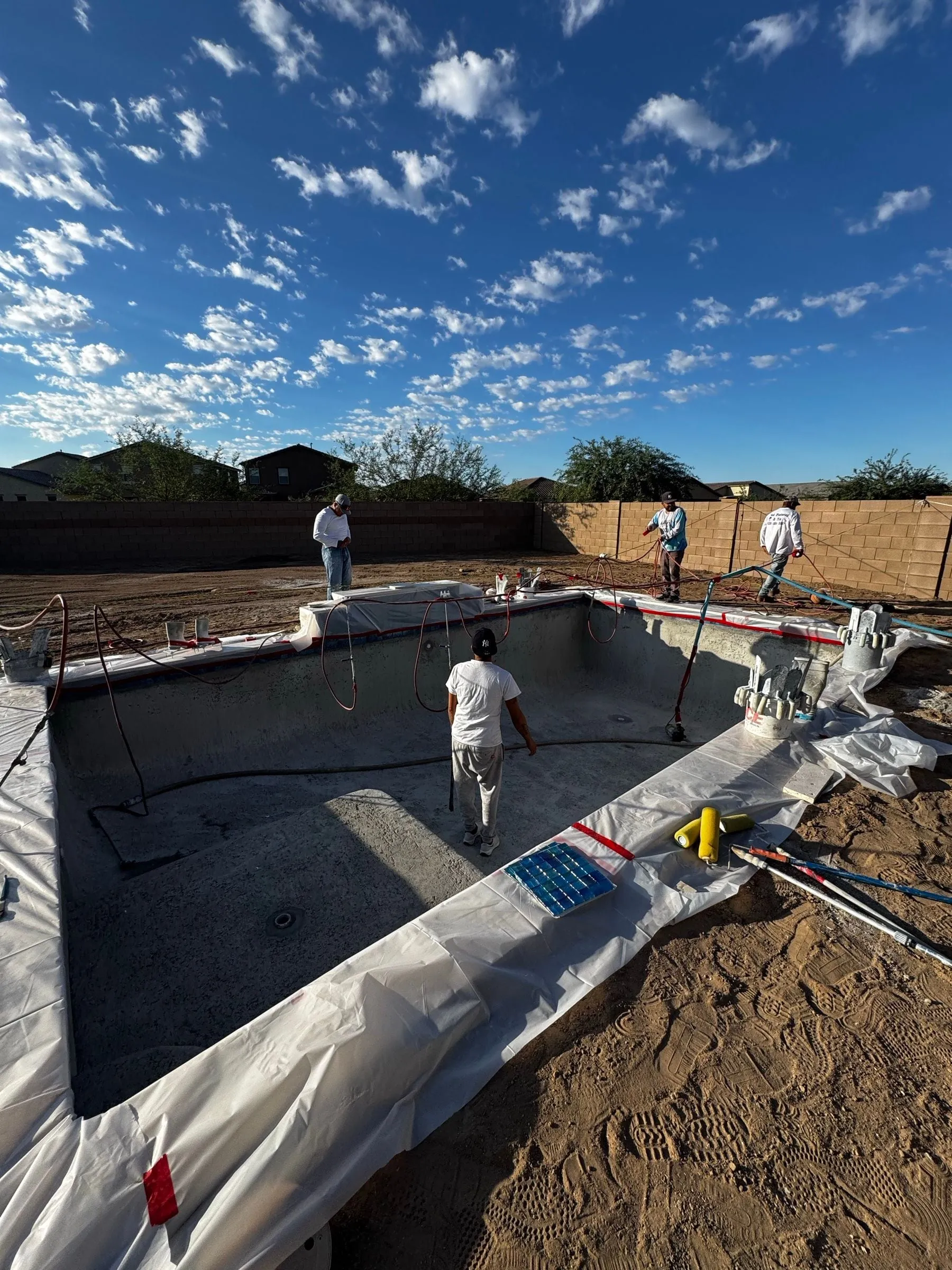 Plaster crew prepares a rectangular pool, with the deck edge protected by plastic sheeting.