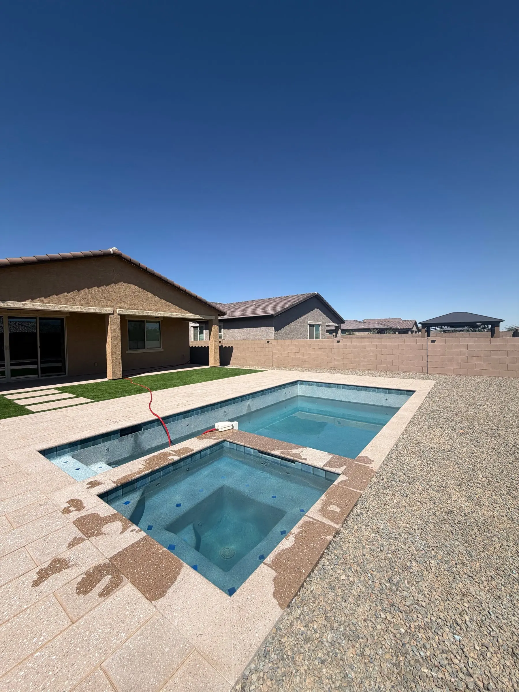 Rectangular pool with an attached spa, light pavers and an exposed aggregate deck border in Gladden Farms.