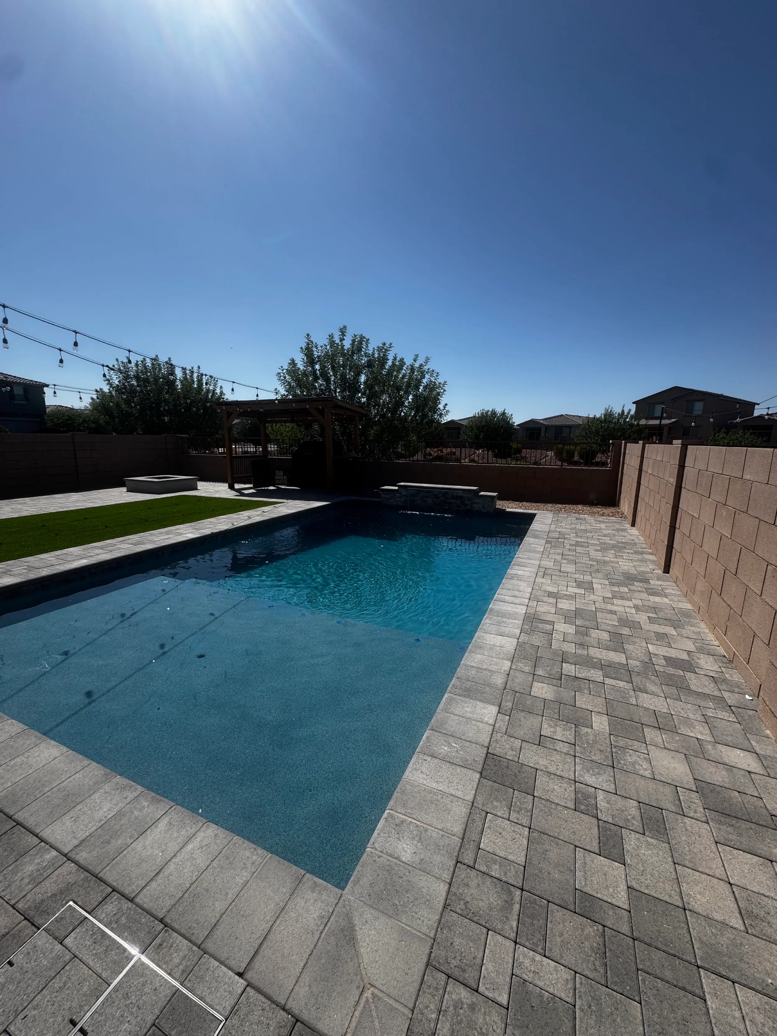 Rectangular pool with a paver deck, raised spa and string lights in a desert backyard