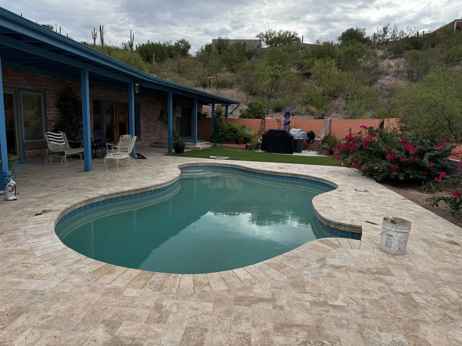 Kidney-shaped pool with a new travertine deck and desert hillside behind it