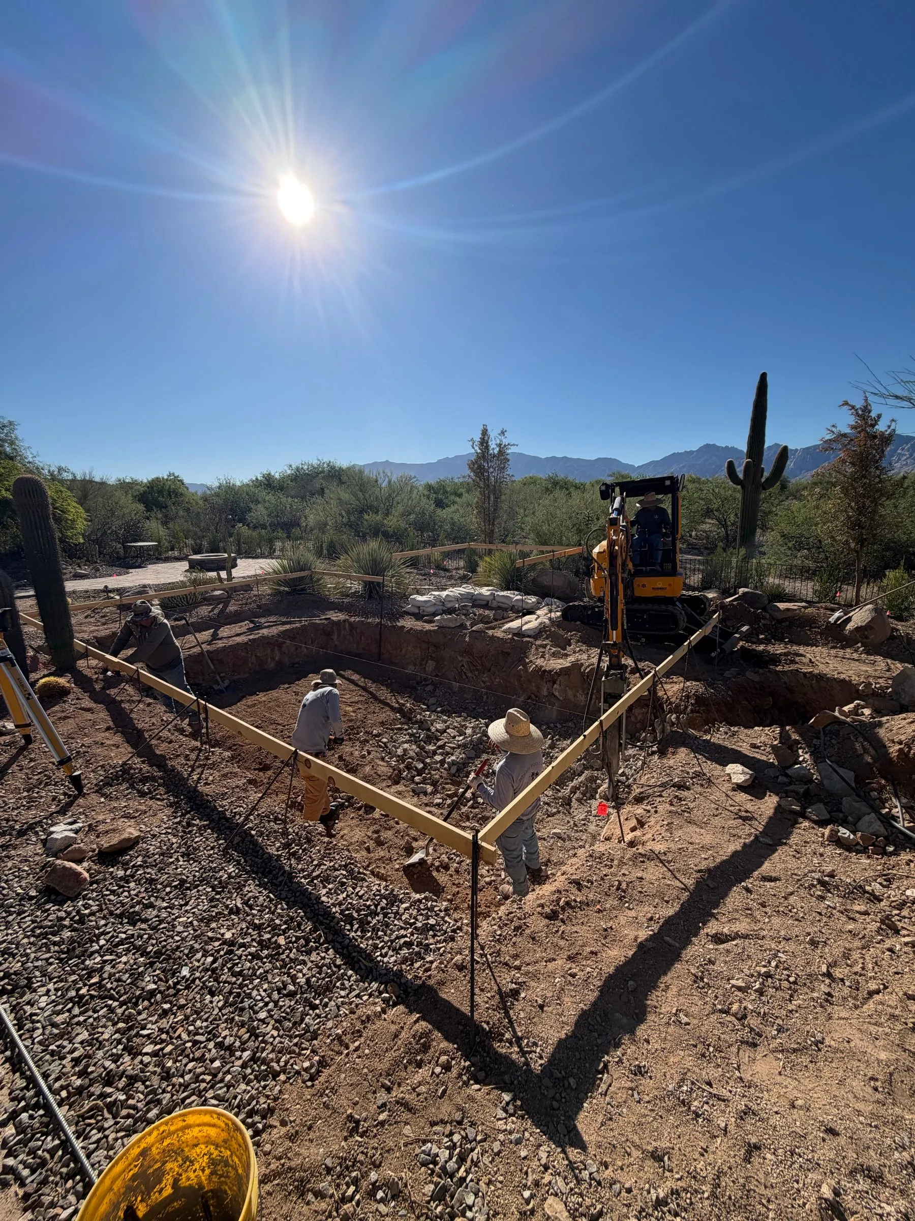 Crew setting layout boards and string lines in a pool excavation near Dove Mountain with mountain views