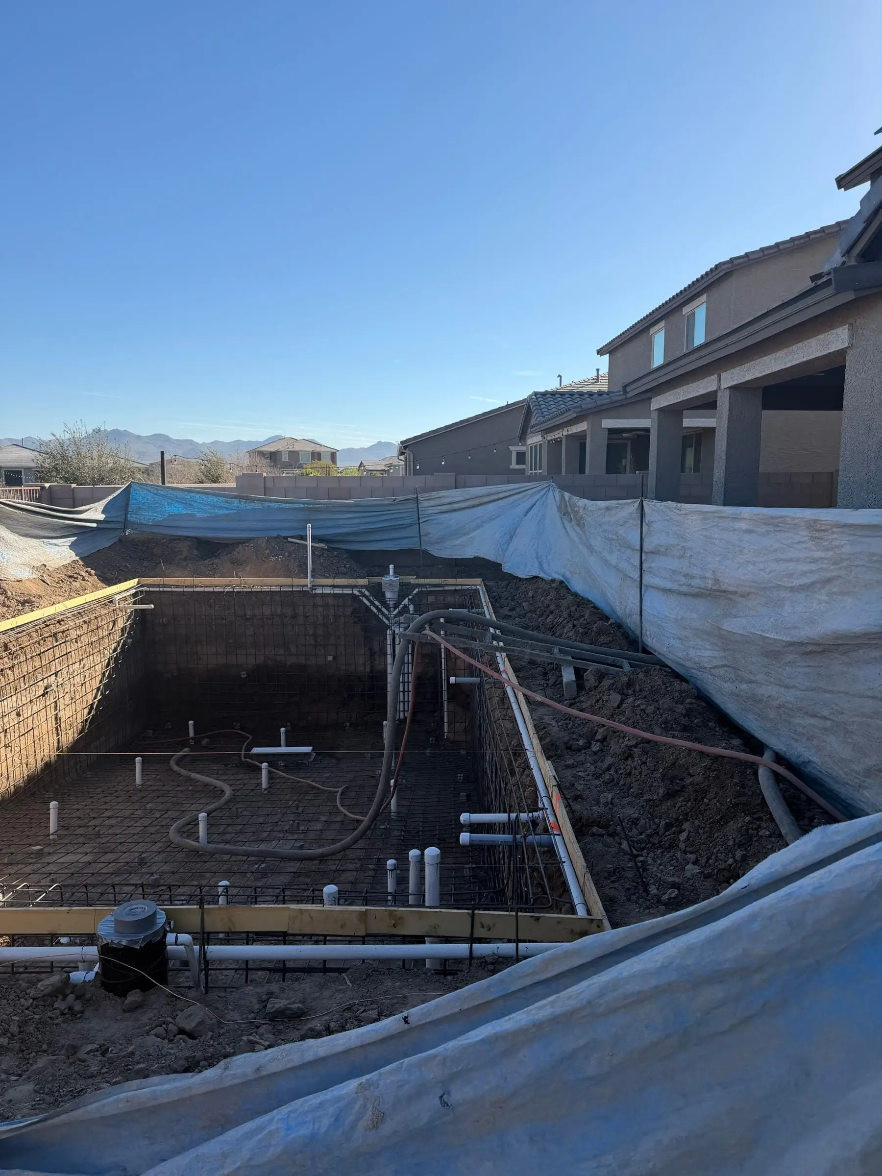 Pool excavation with rebar and plumbing, its edges covered in plastic for shotcrete.