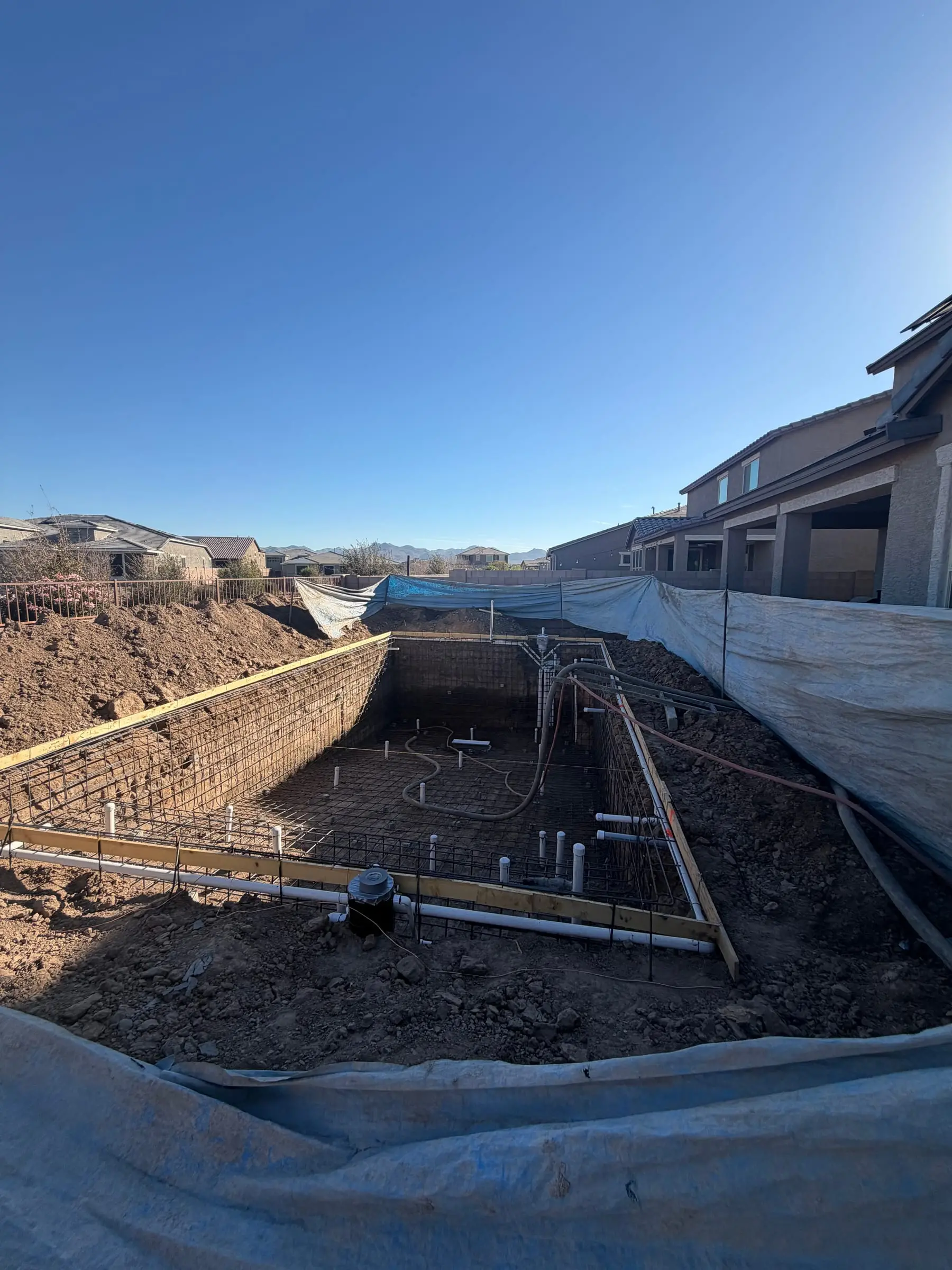 Rectangular pool excavation with wood forms, rebar and plumbing, with plastic protecting the side yard, Gladden Farms in Marana, AZ.