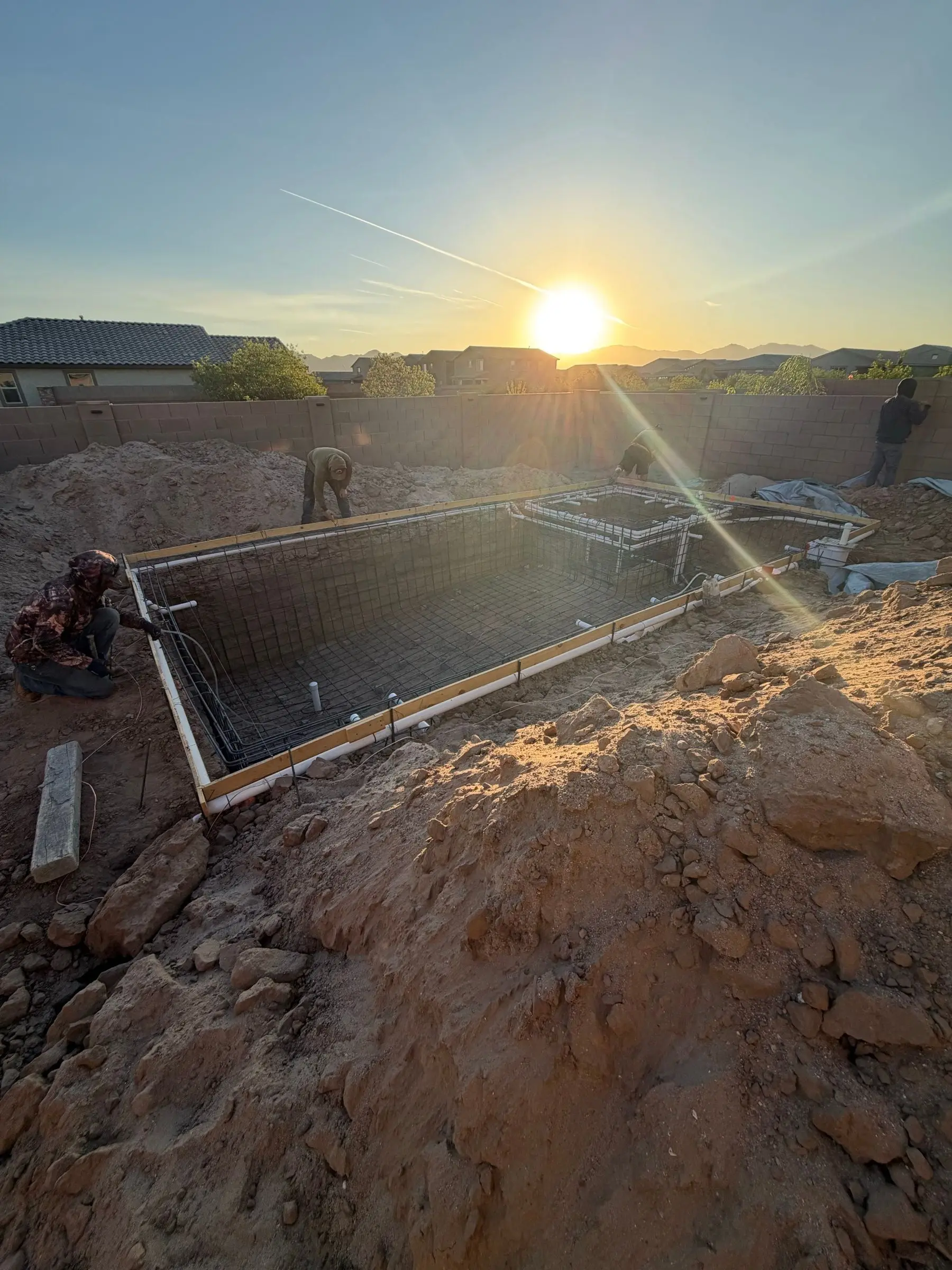 Sun setting over a rebar-lined pool excavation in Gladden Farms with fresh dirt piled in front.