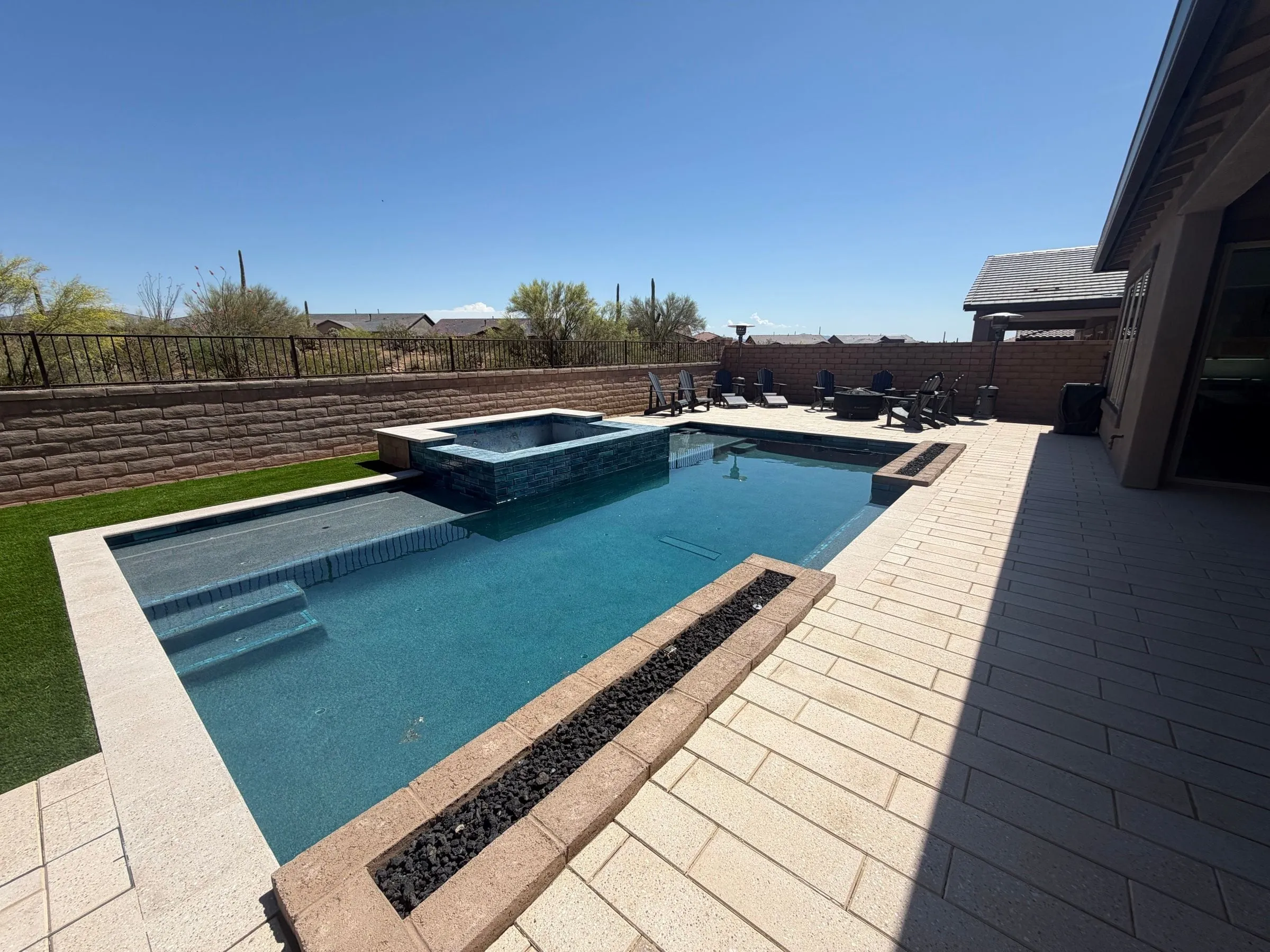 Rectangular pool with a linear fire trough, raised tiled spa and light paver deck.