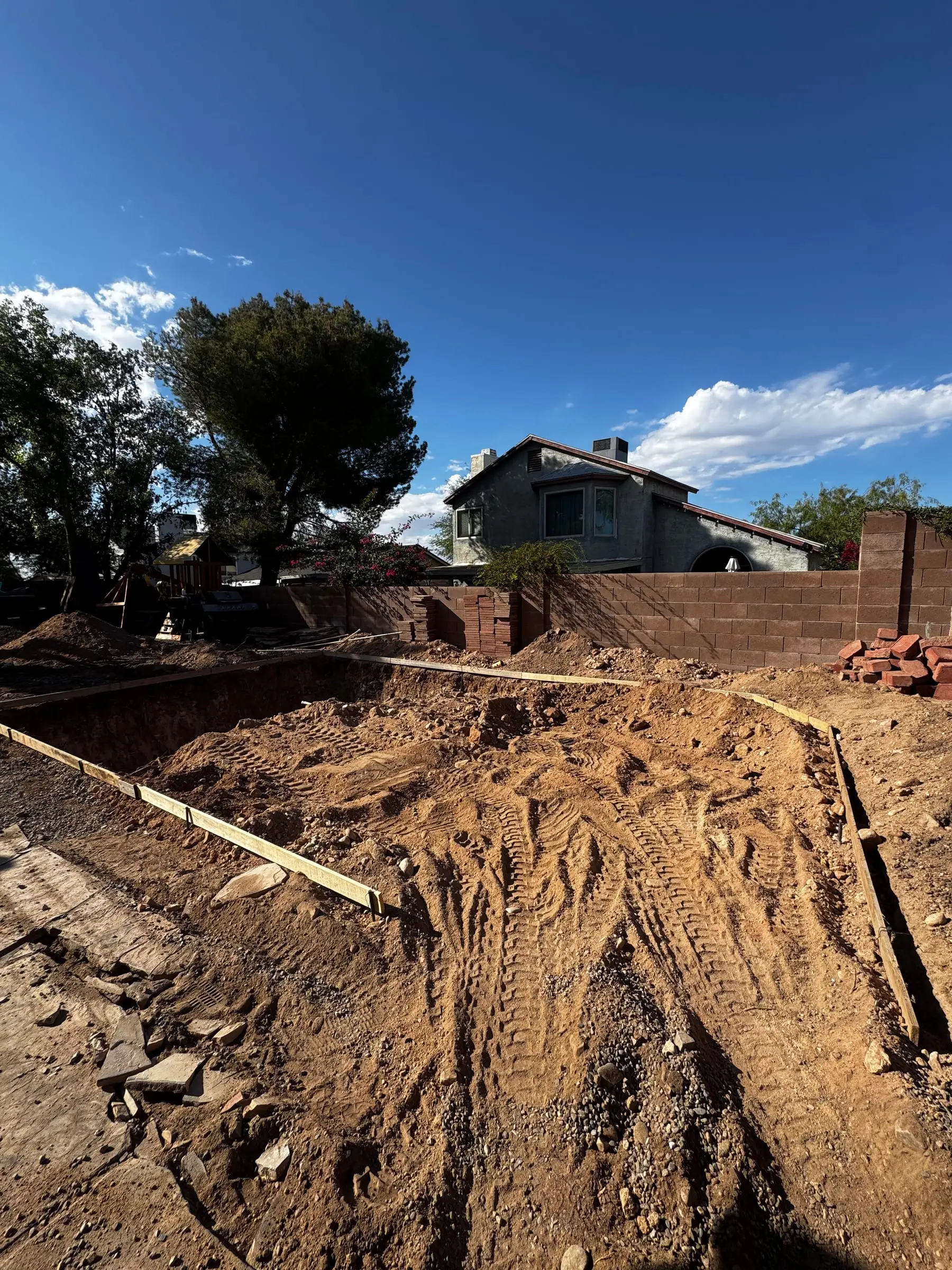 Wood forms and the first cuts of a pool excavation in an established backyard.