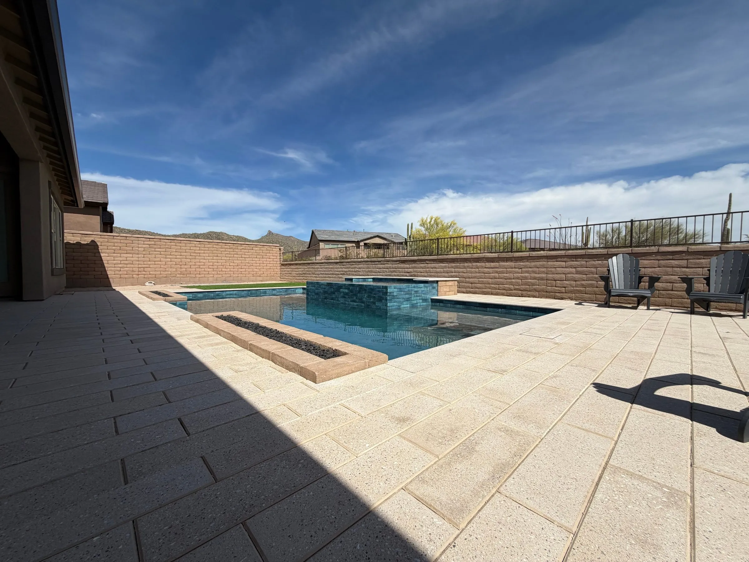 Rectangular pool with a raised spa and linear fire trough on a wide light paver deck in Marana.