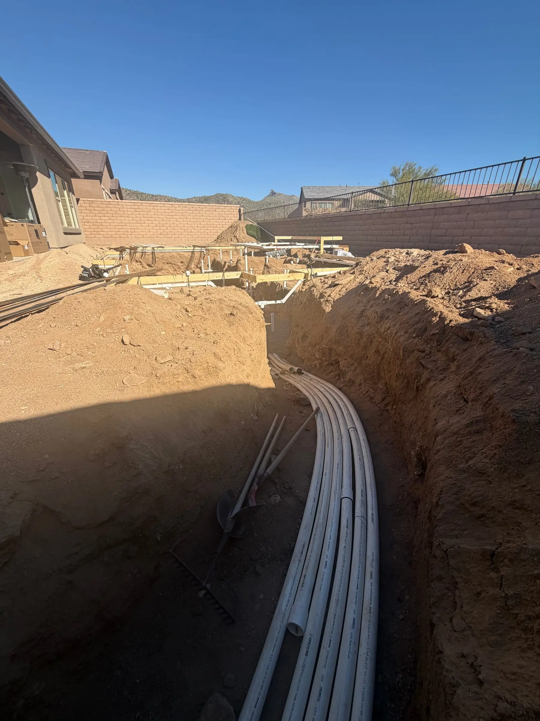 Bundled pool plumbing lines laid in a trench beside a fresh pool excavation, Marana, AZ.