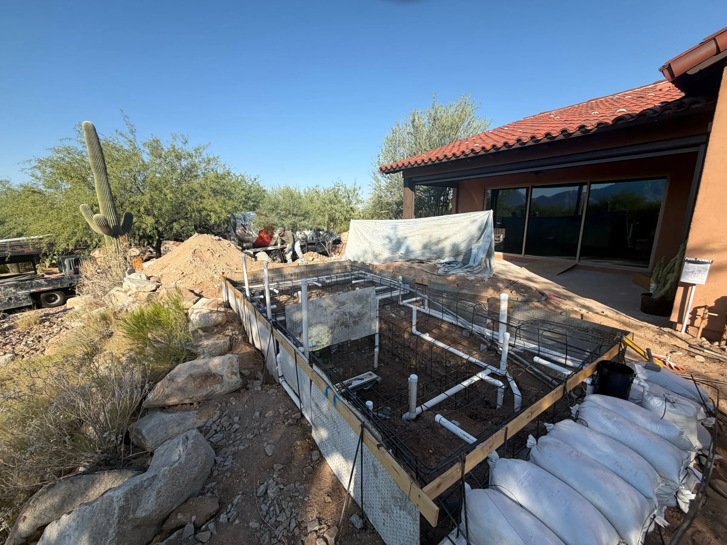 Rectangular pool excavation with rebar and plumbing beside a tile-roofed desert home