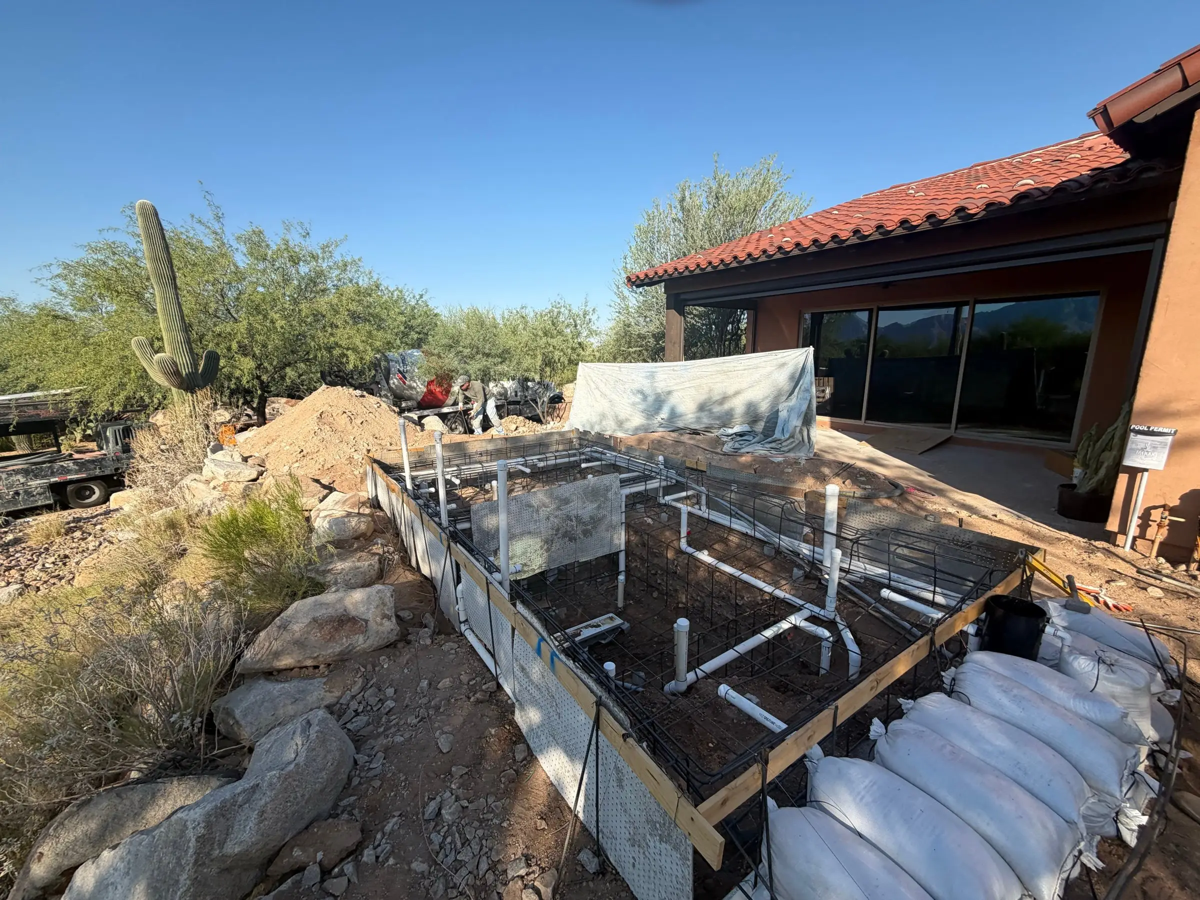 Rectangular pool excavation with rebar and plumbing beside a tile-roofed desert home