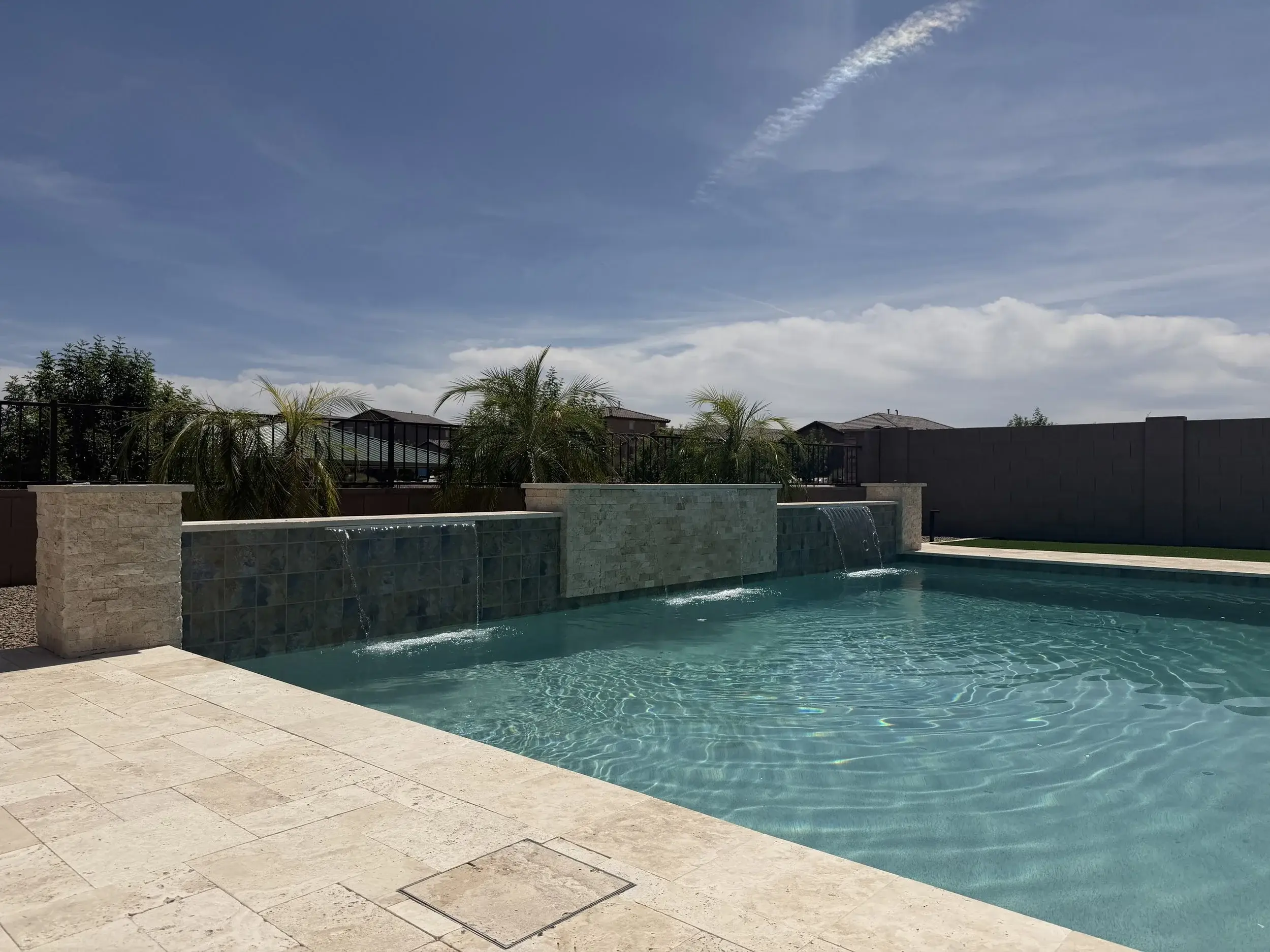 Rectangular pool with tiled raised wall, two sheer descents and stacked stone pillars on travertine in Tucson.