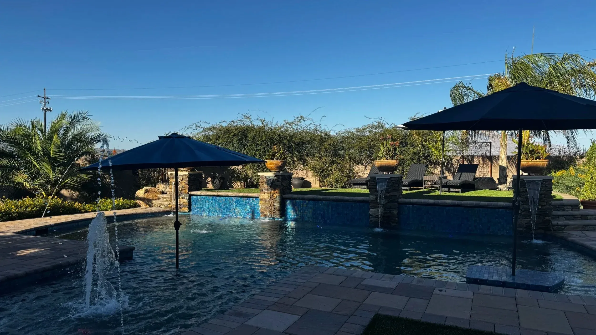 Pool with stone columns, deck jets and patio umbrellas at sunset