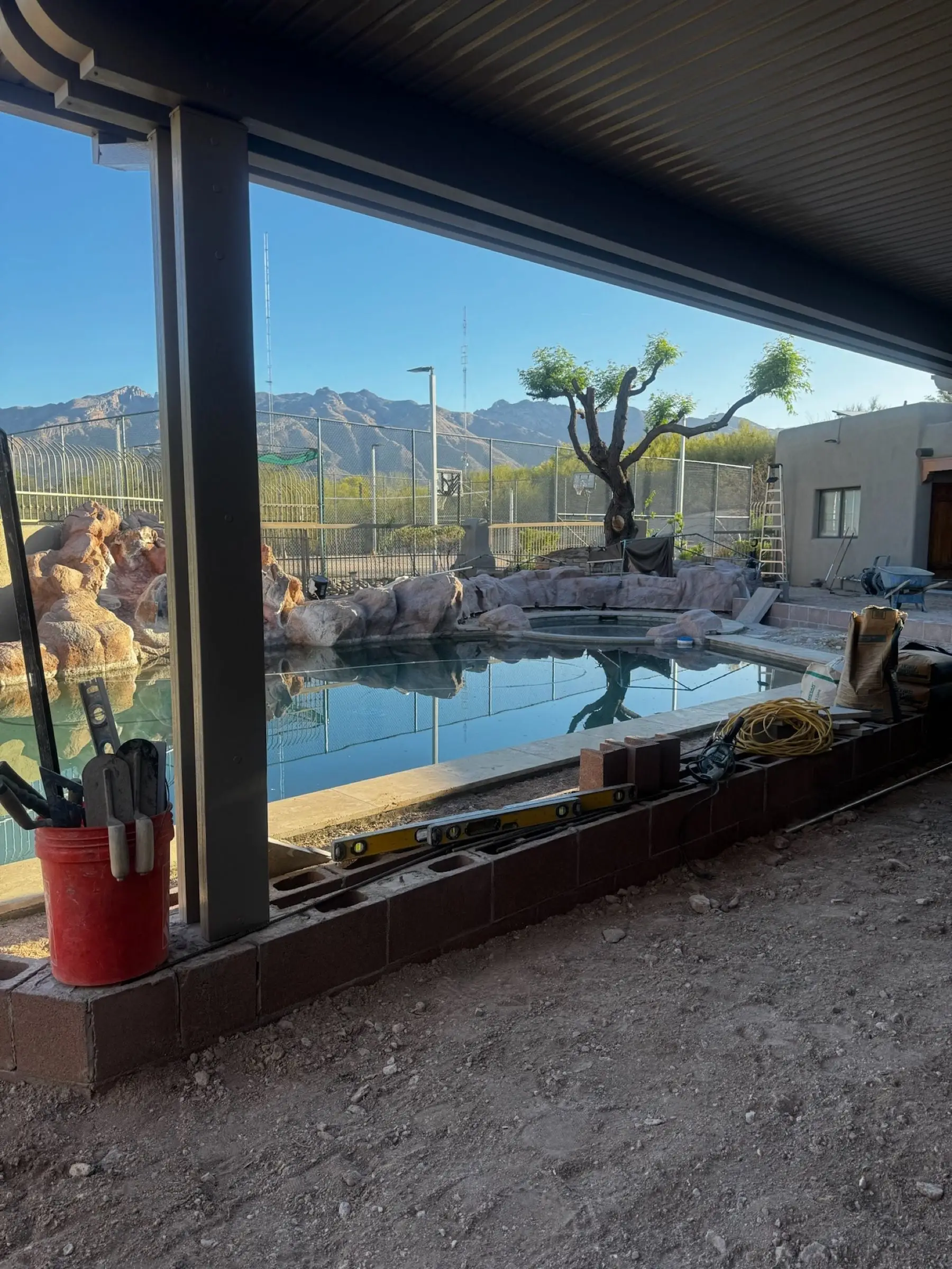 Covered patio view of a pool with a natural rock waterfall during deck renovation in the Catalina Foothills.