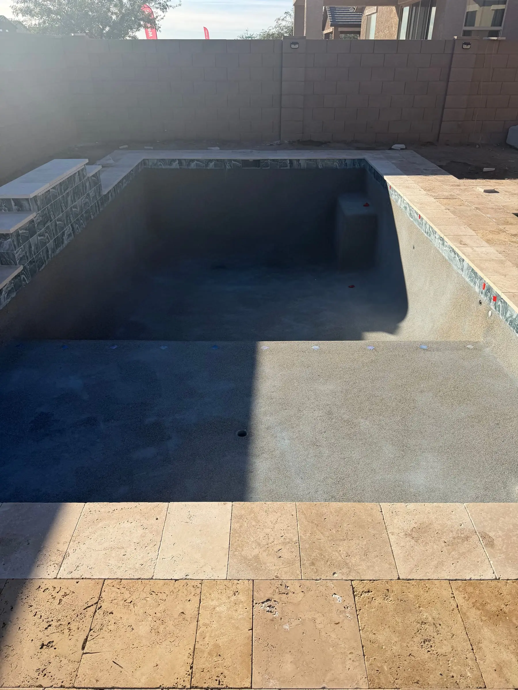 Inside an empty pool shell with mosaic waterline tile, a raised wall and a travertine deck, Marana, AZ.