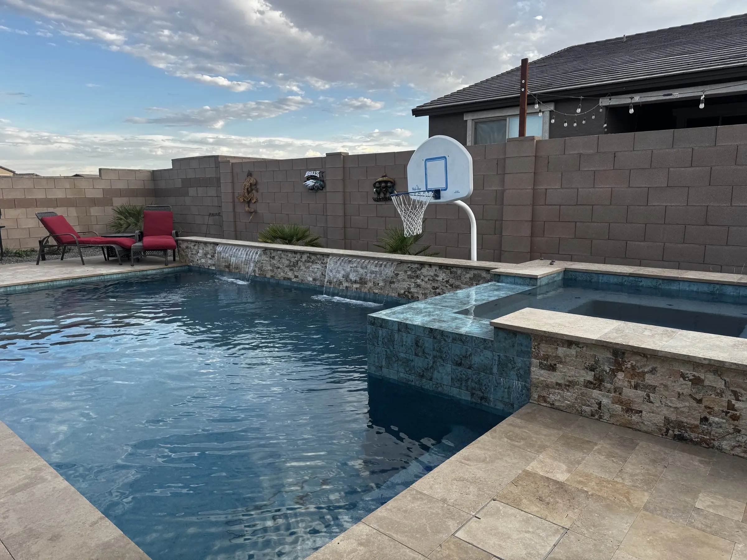 Pool with stacked stone raised wall, twin sheer descents and raised spa spillover on travertine.