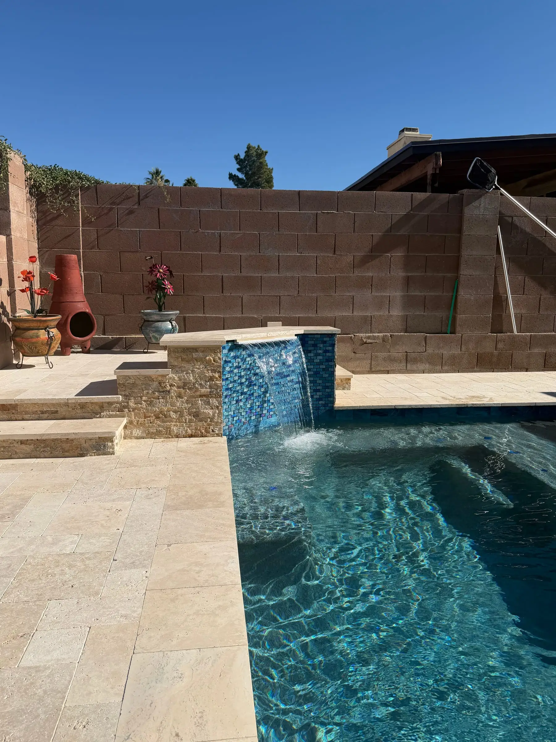 Finished pool with a tiled water feature spilling into the water and a travertine deck.
