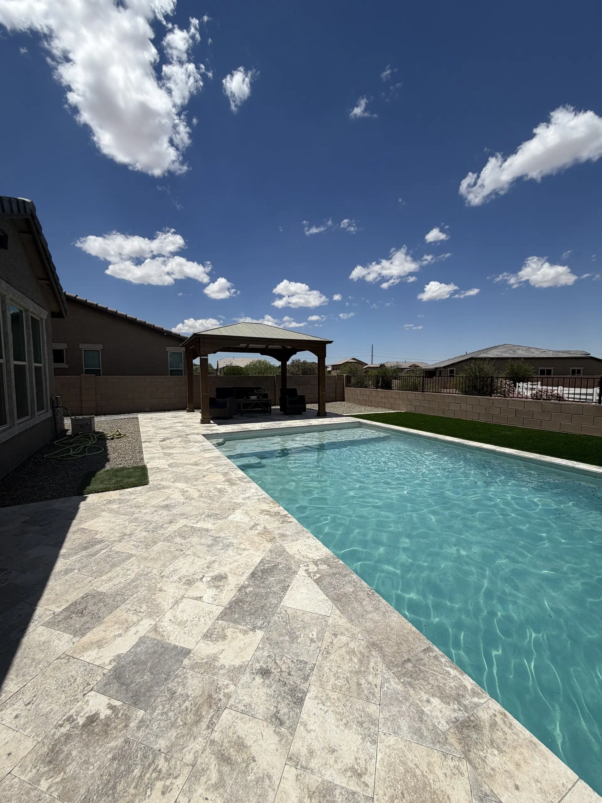 Rectangular pool with travertine deck, wood gazebo and artificial turf under a blue Tucson sky.