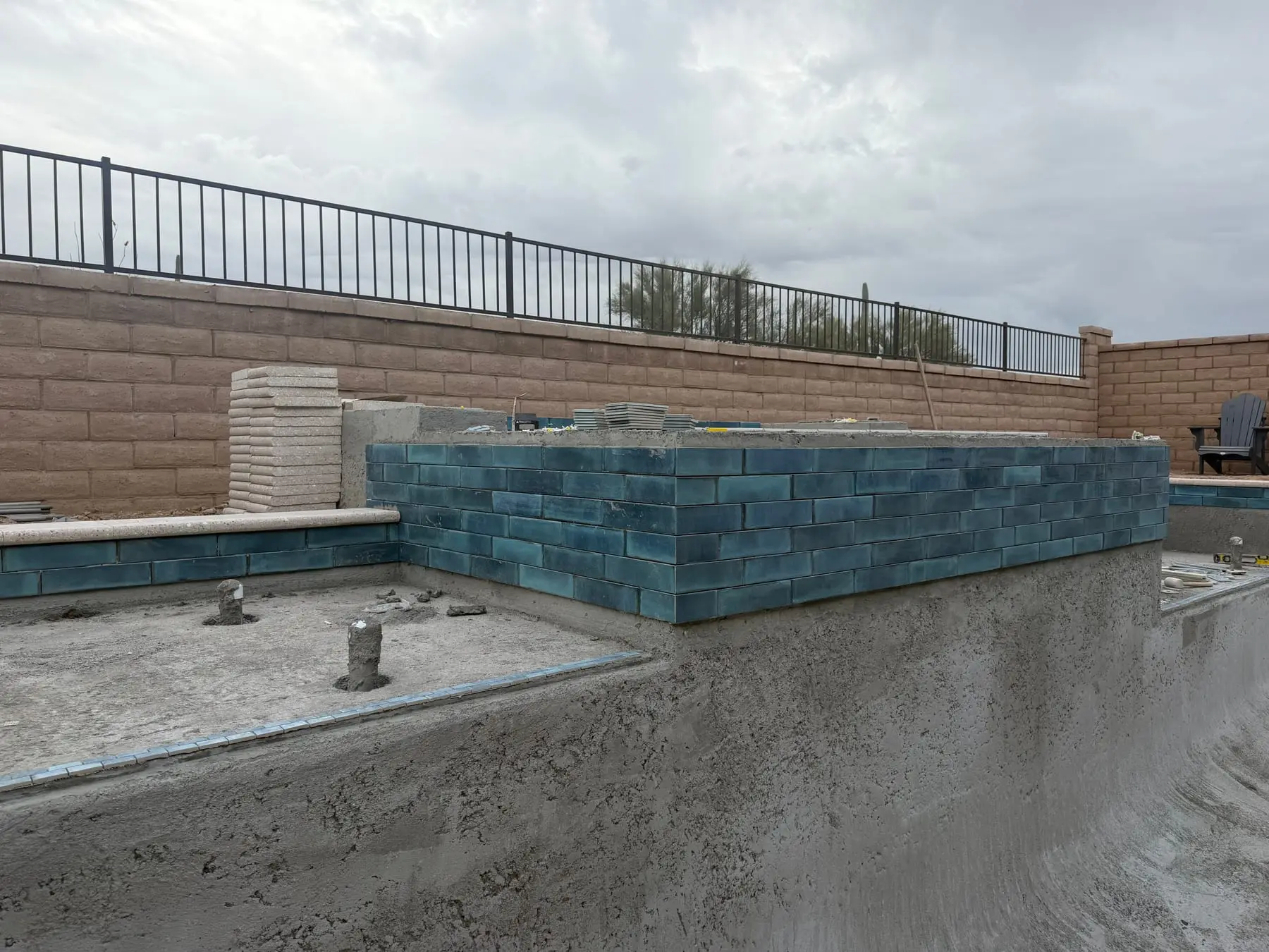 Dark glass tile on the face of a raised spa above a new pool shell.