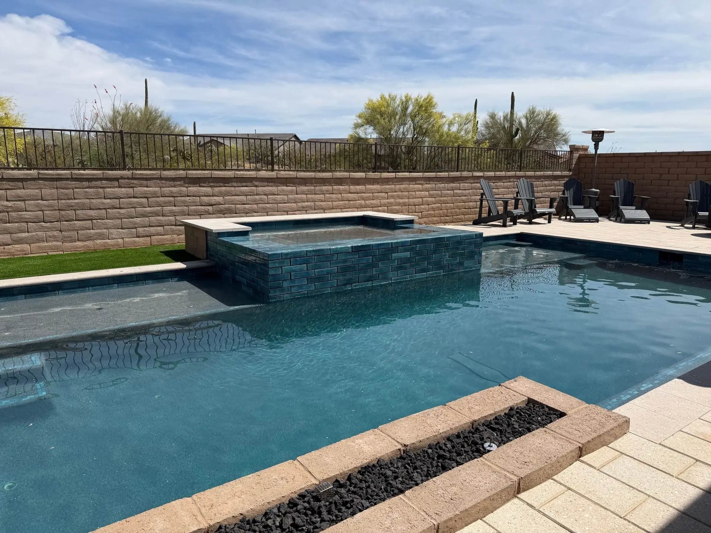 Raised spa clad in dark tile above a pool, with a lava rock fire trough in front.