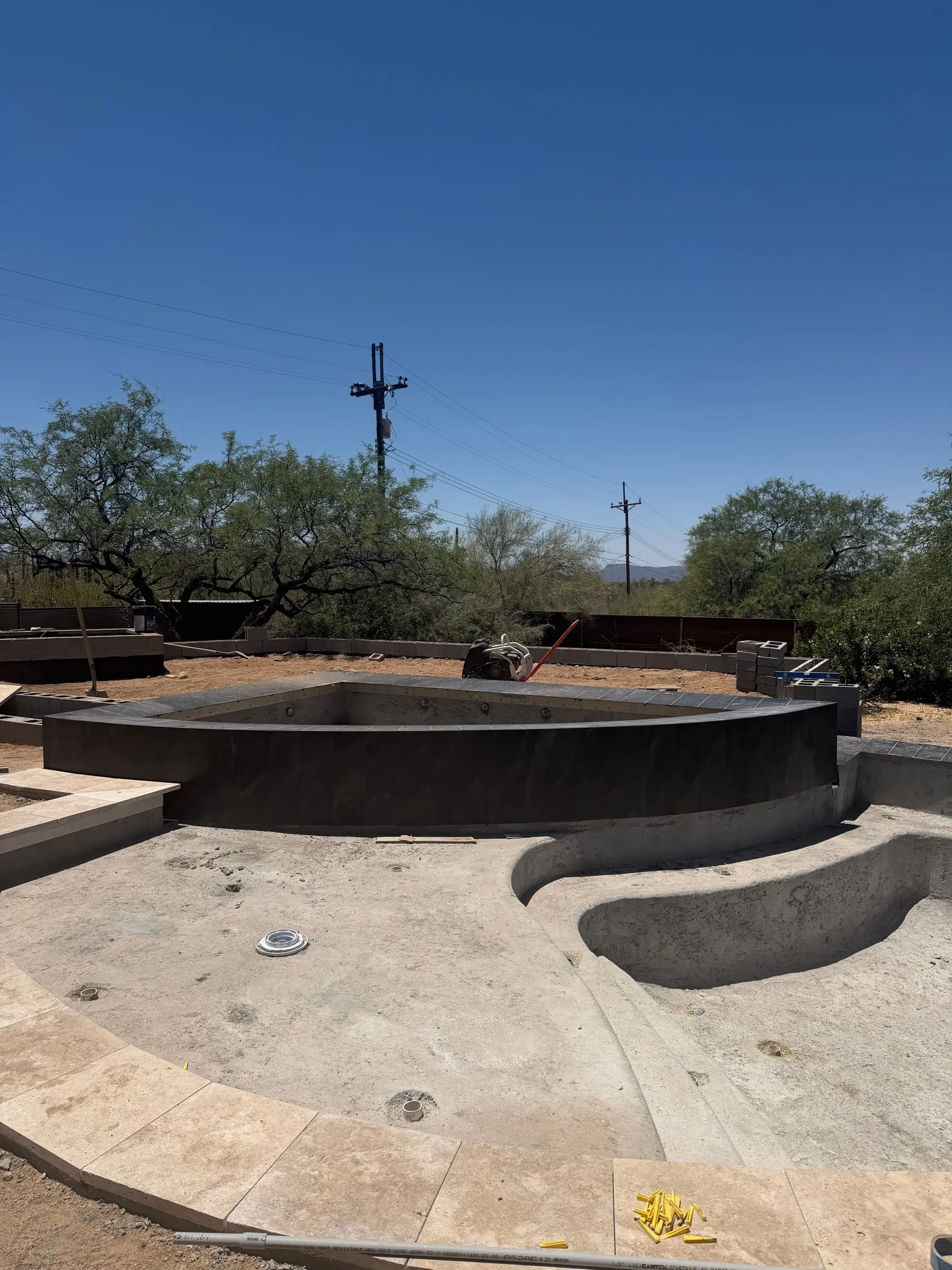 Raised spa wrapped in dark tile above a pool shell with a curved bench and travertine coping
