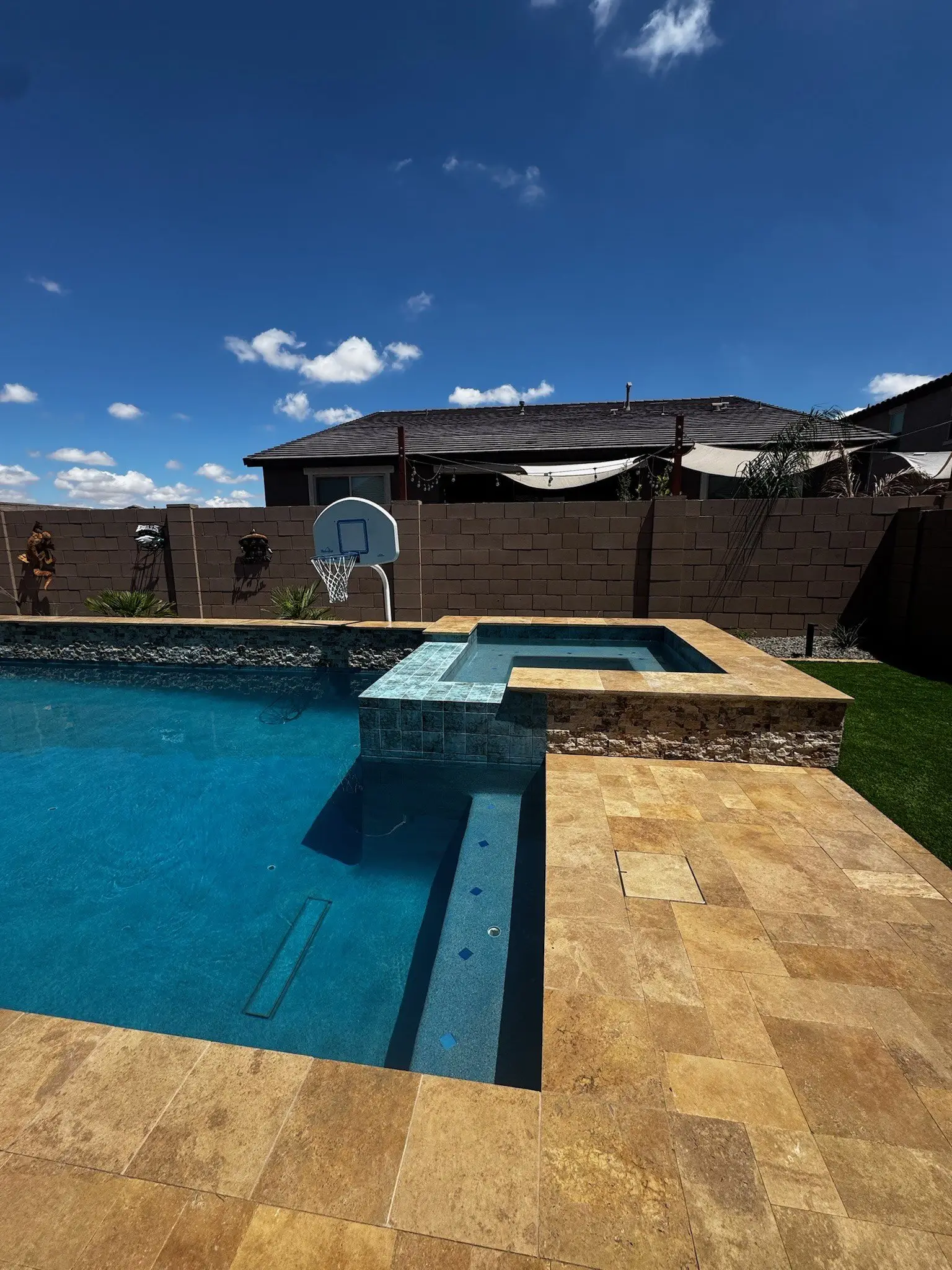Raised spa with tile spillover and stacked stone base beside a travertine deck and turf.