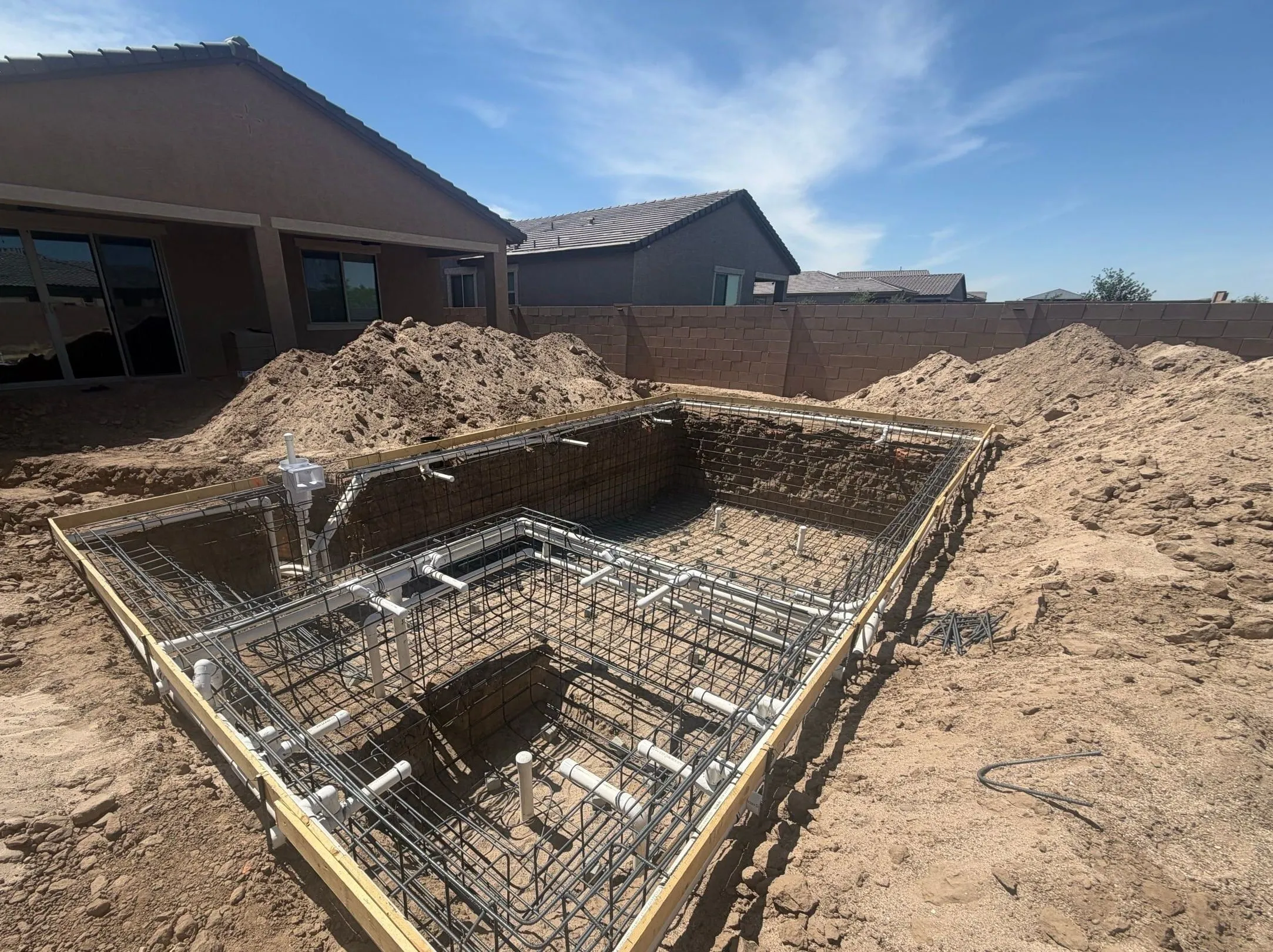 Rebar and plumbing set in a compact rectangular pool excavation framed with wood forms.