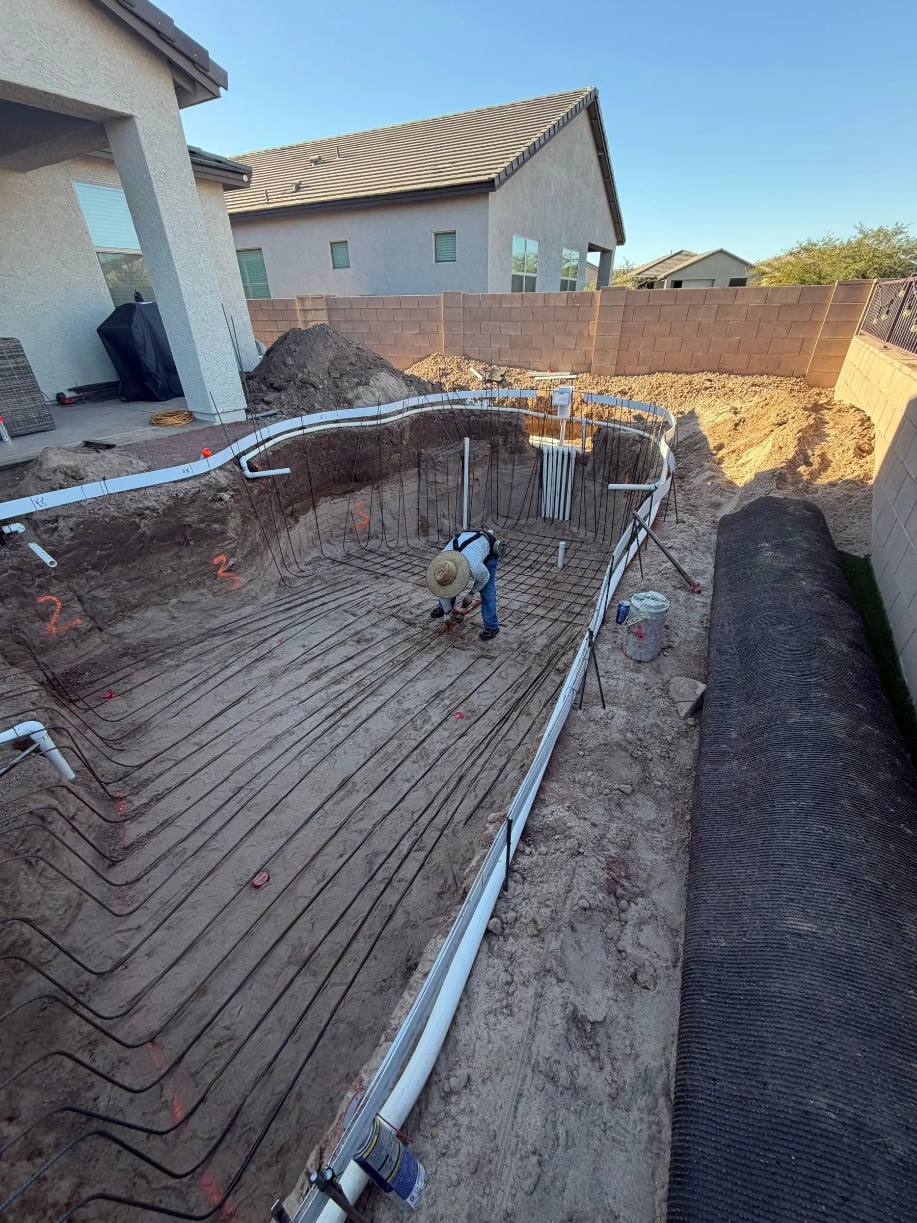 Rebar grid lining a freeform pool excavation as a crew member ties steel.