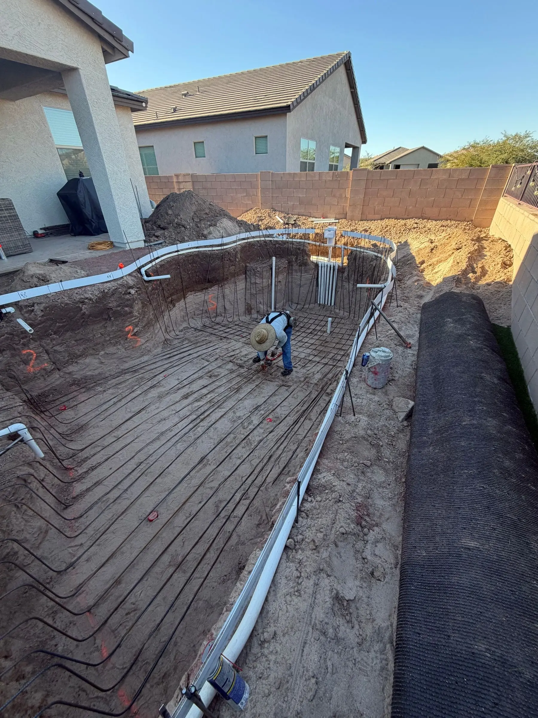 Rebar grid lining a freeform pool excavation as a crew member ties steel, Marana, AZ.