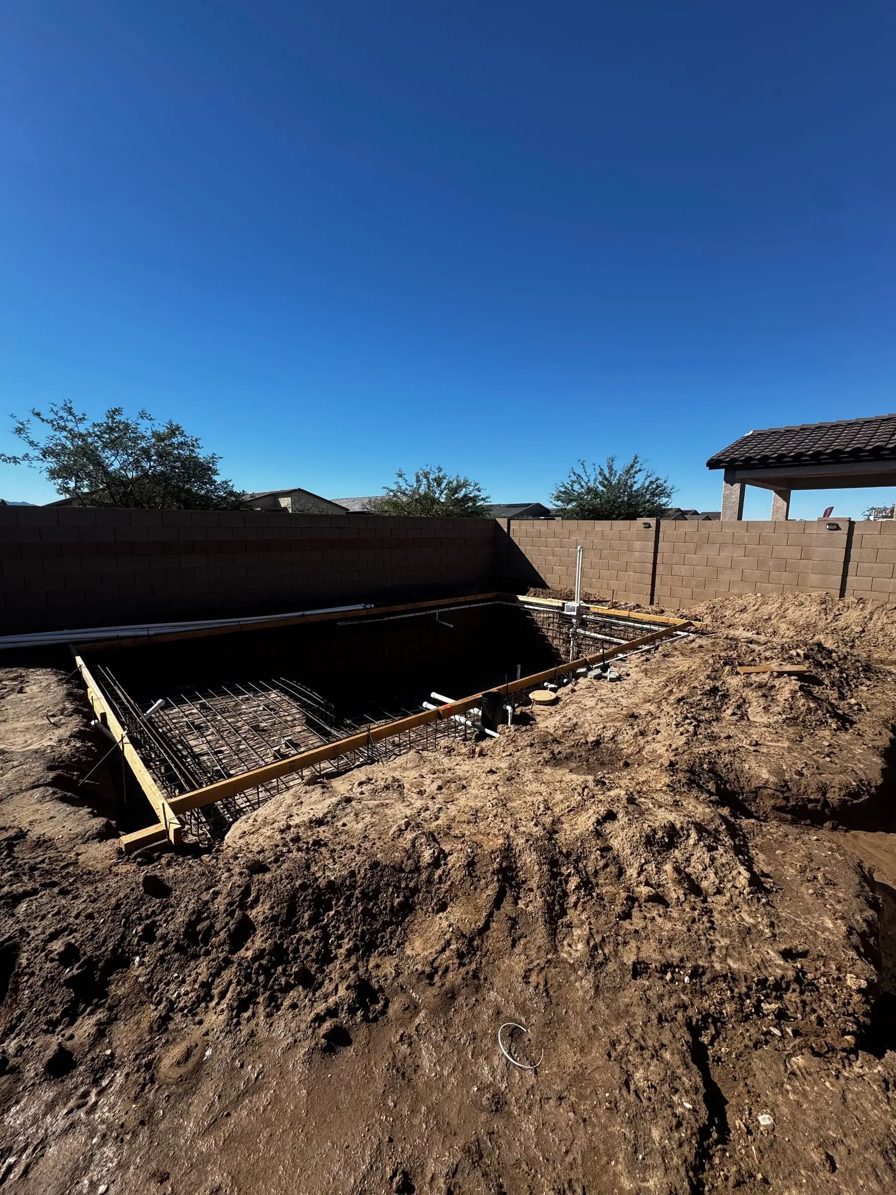 Rebar grid tied across a rectangular pool excavation beside a block wall in Marana.