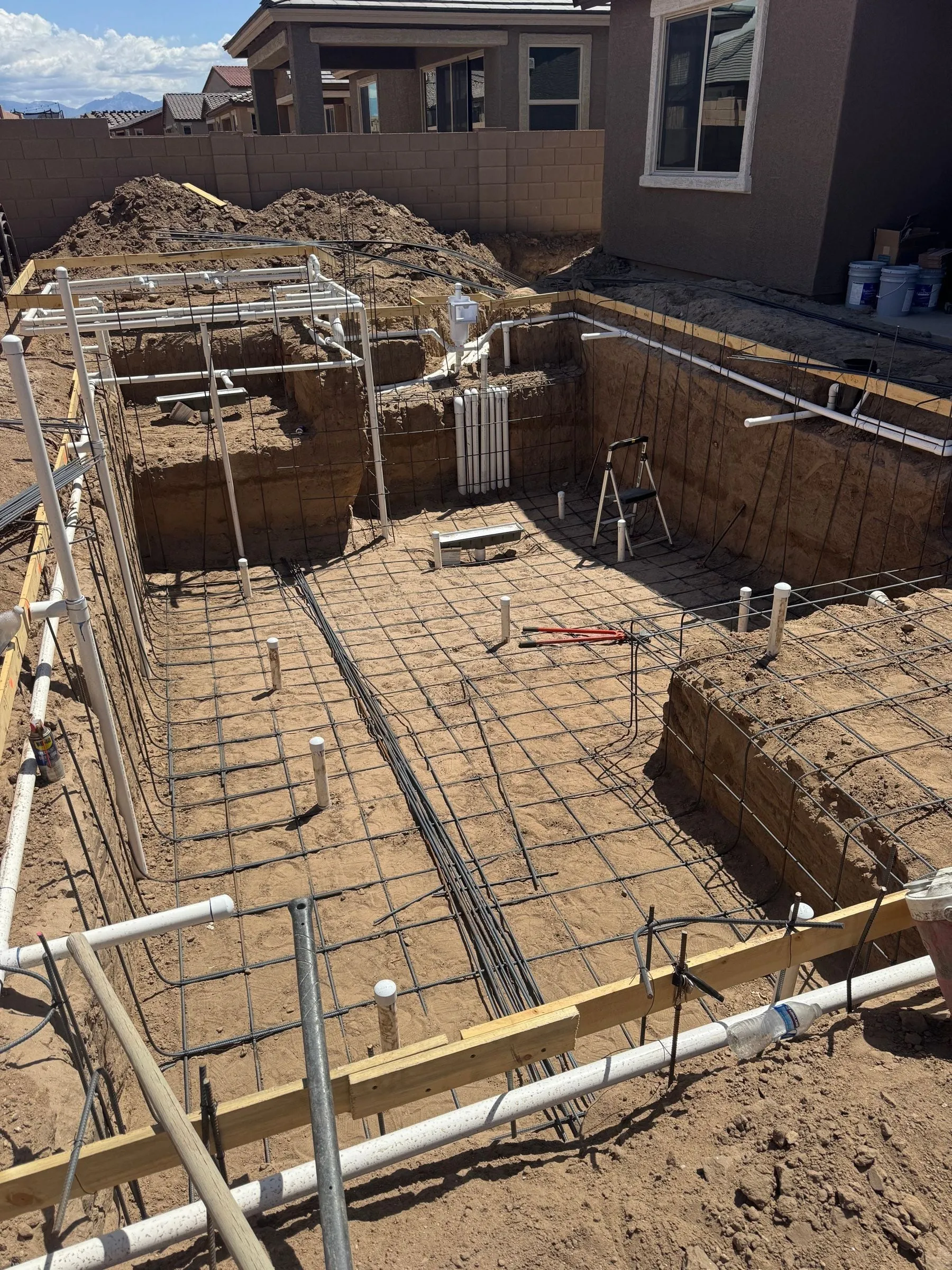 Steel rebar grid tied throughout a rectangular pool excavation with plumbing stub-outs in place.