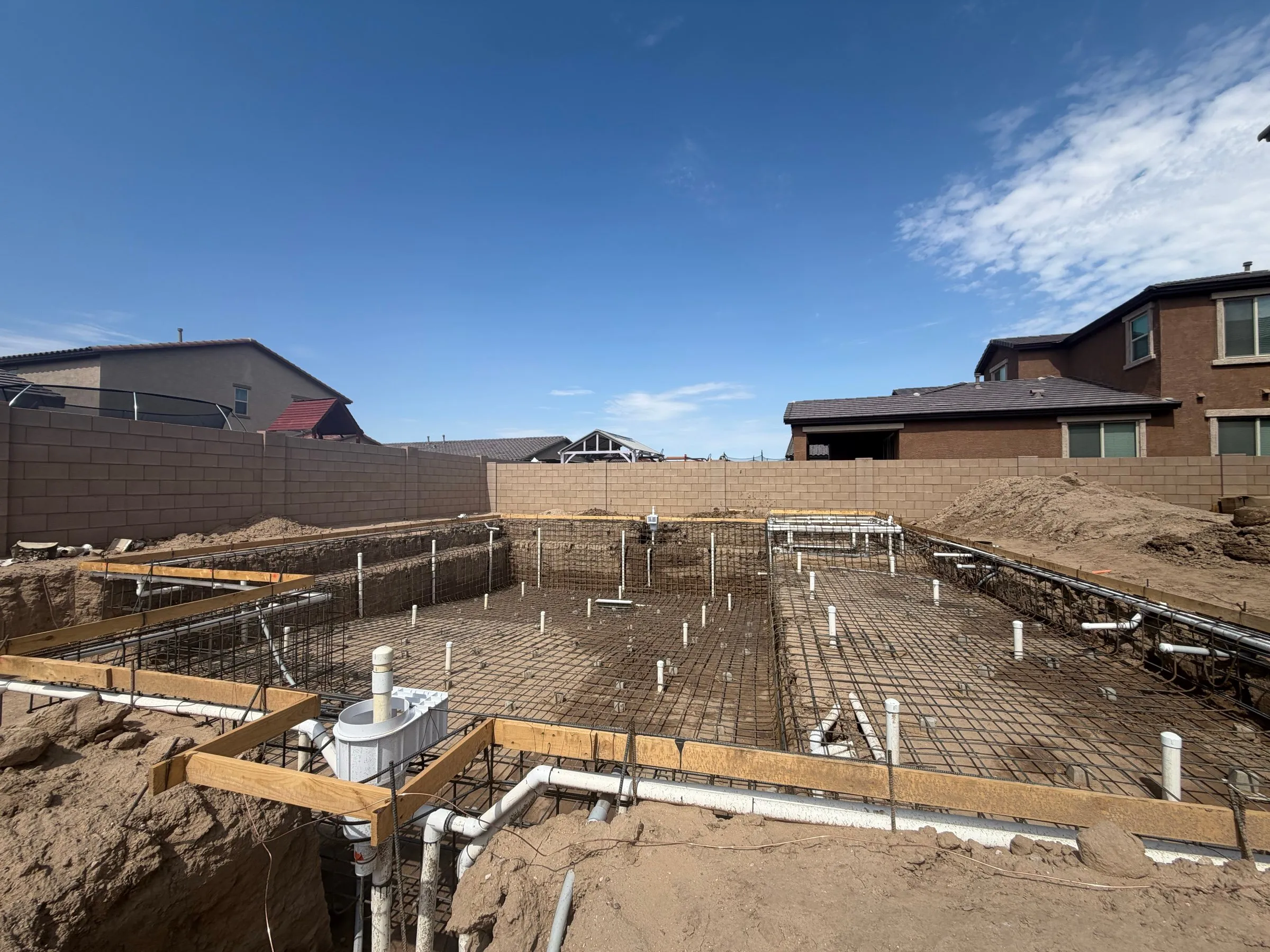 Rebar grid and plumbing stubs in a large rectangular pool excavation in Marana.