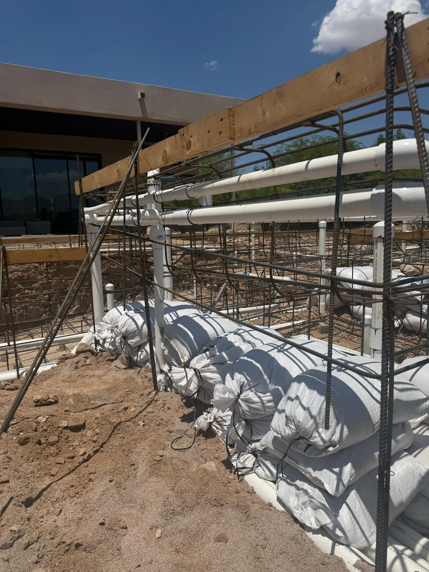 Pool plumbing manifold and rebar along a wood form next to a modern desert home