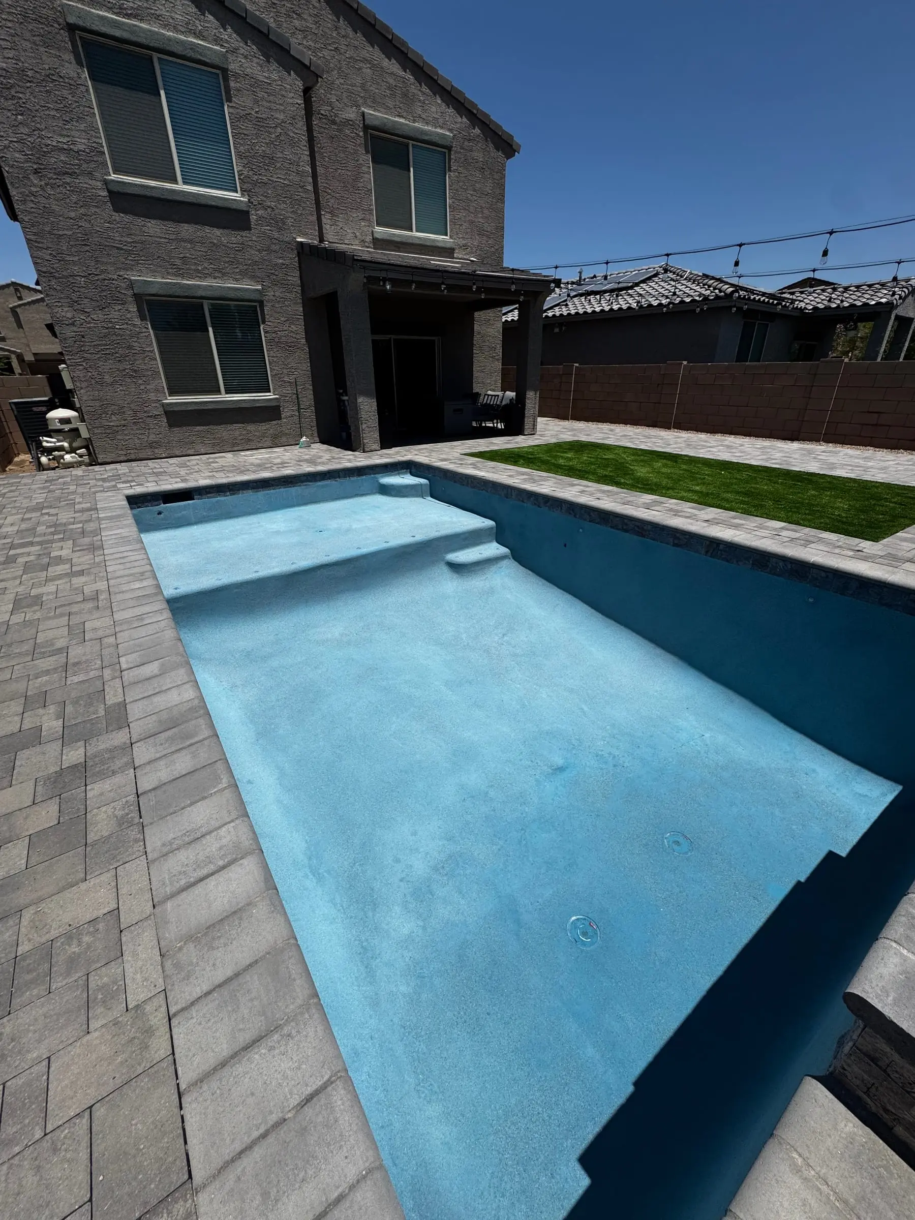 Newly filled rectangular pool with entry steps, gray paver deck and turf behind a two-story home, Marana, AZ.