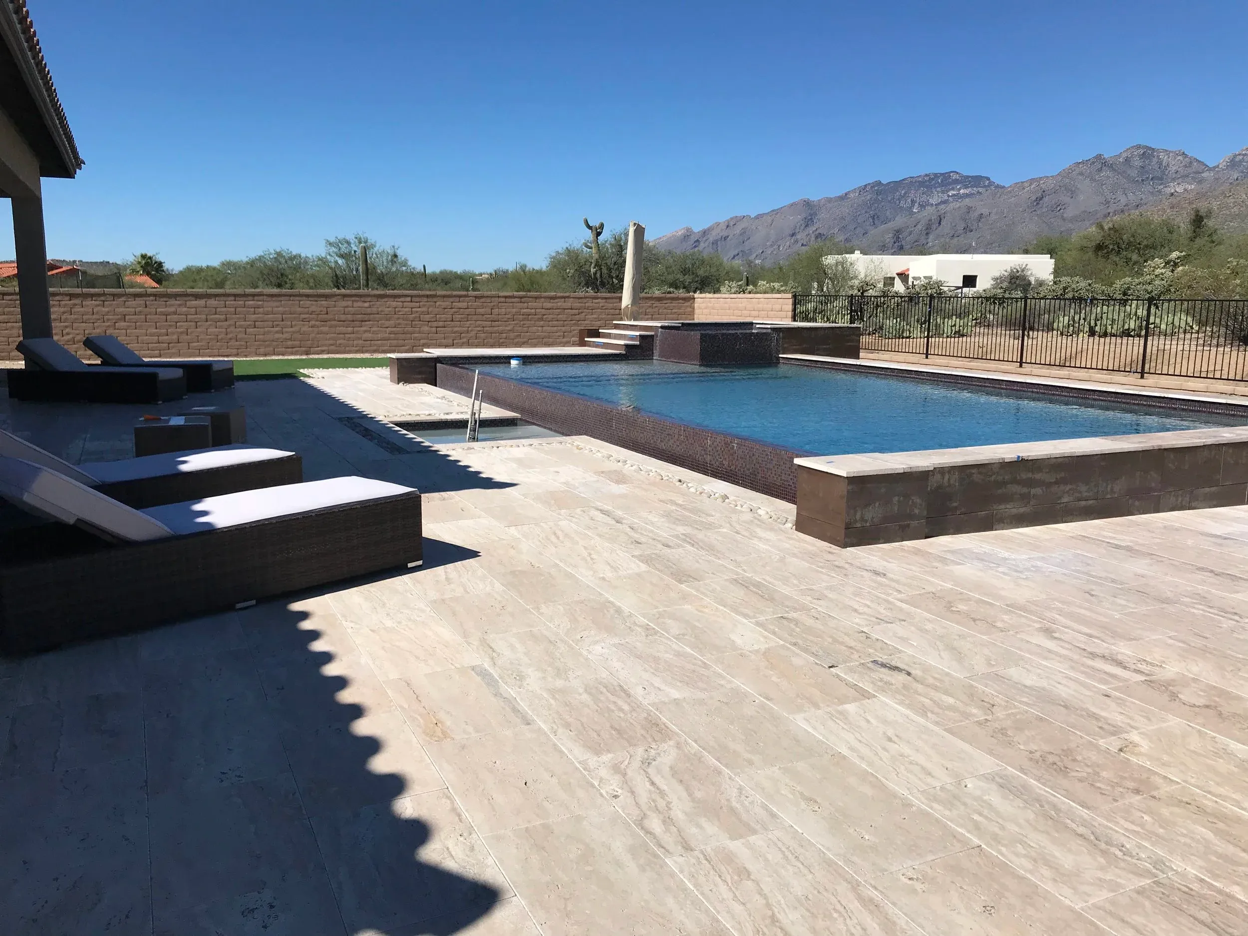 Rectangular pool with raised tile edge, raised spa and wide travertine deck beneath desert mountains.