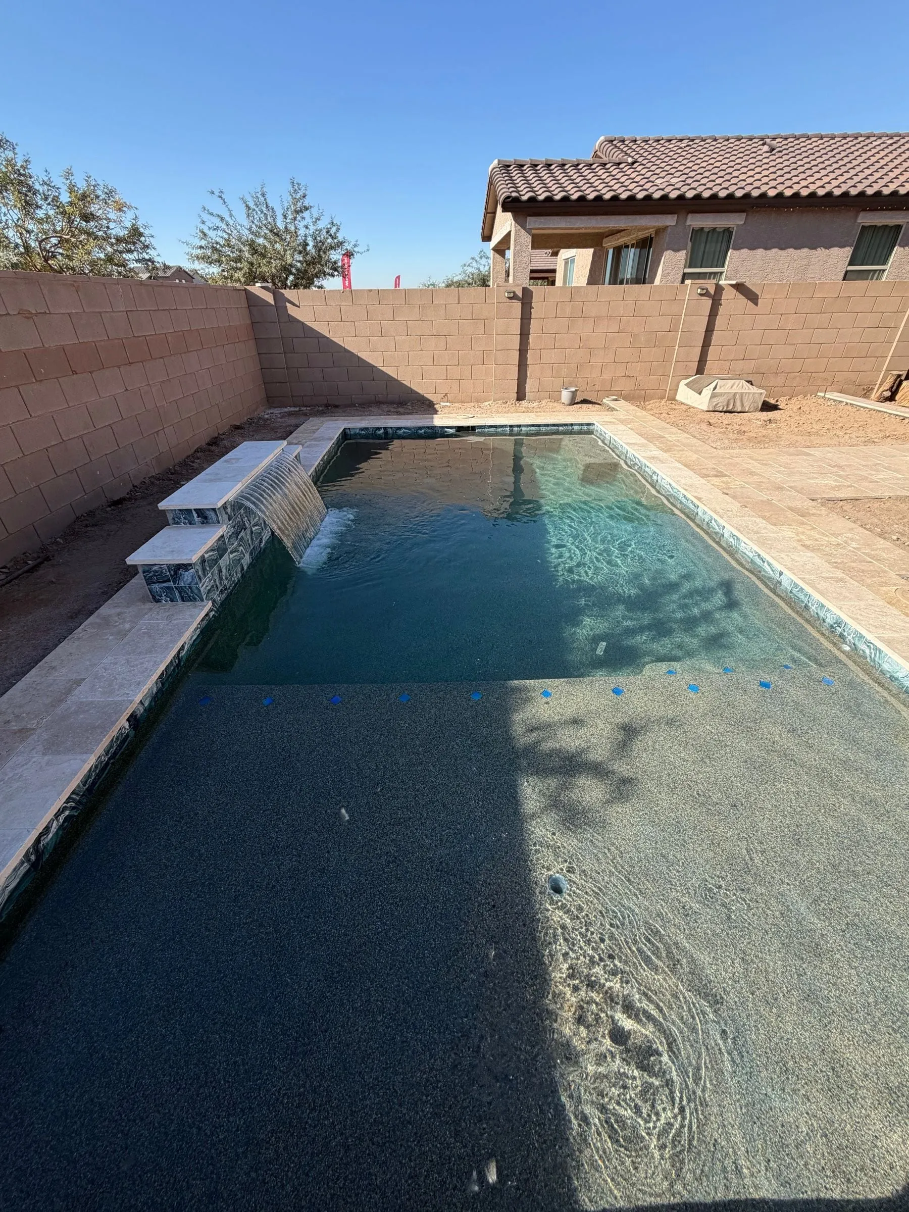 Rectangular pool with sheer descent water features and dark plaster, edged in travertine.