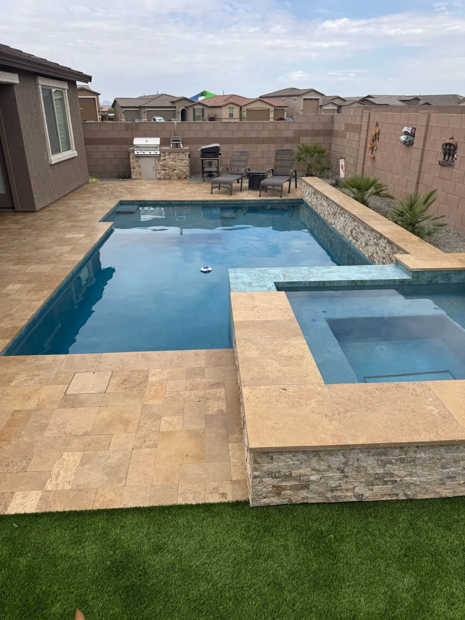 Rectangular pool with raised spa, stacked stone wall, travertine deck and built-in grill island.