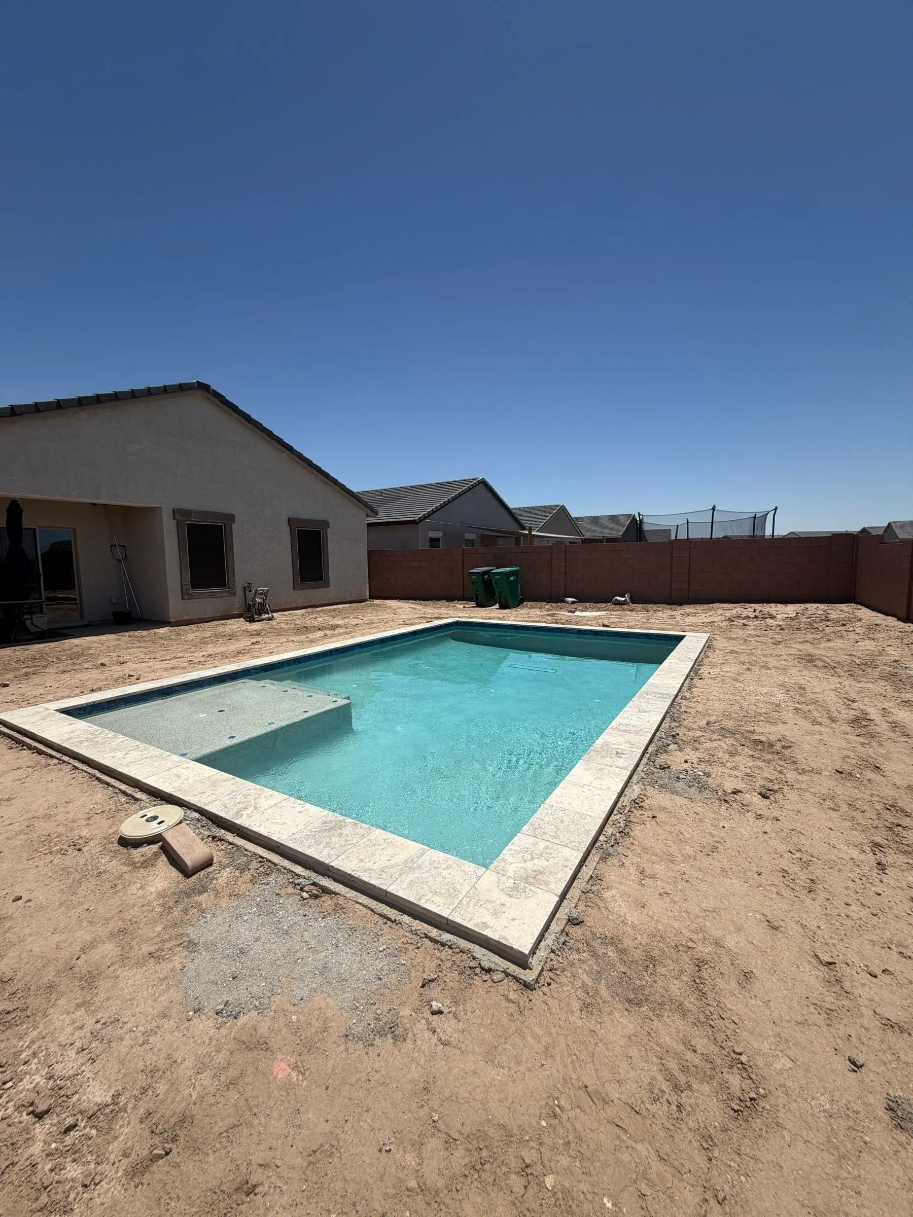 Rectangular pool with a tanning ledge and travertine coping, newly filled before landscaping.
