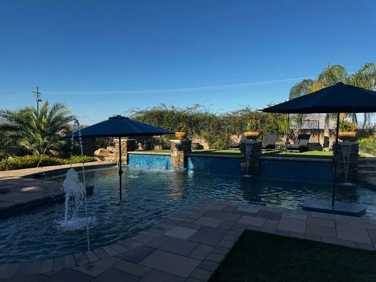 Pool with stone columns, deck jets and blue patio umbrellas at sunset