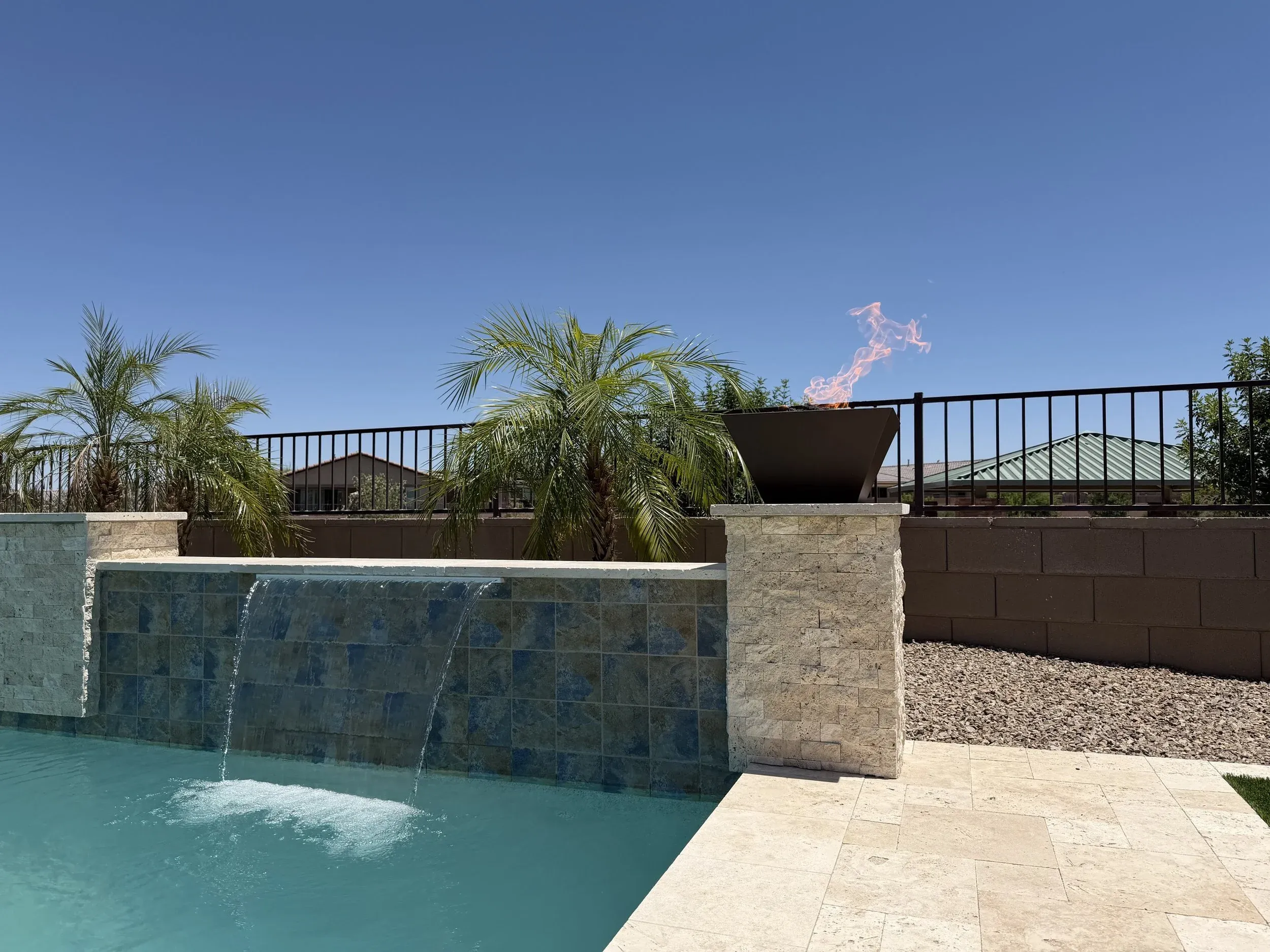Blue tile sheer descent wall and fire bowl on a stacked stone pillar beside a travertine deck.