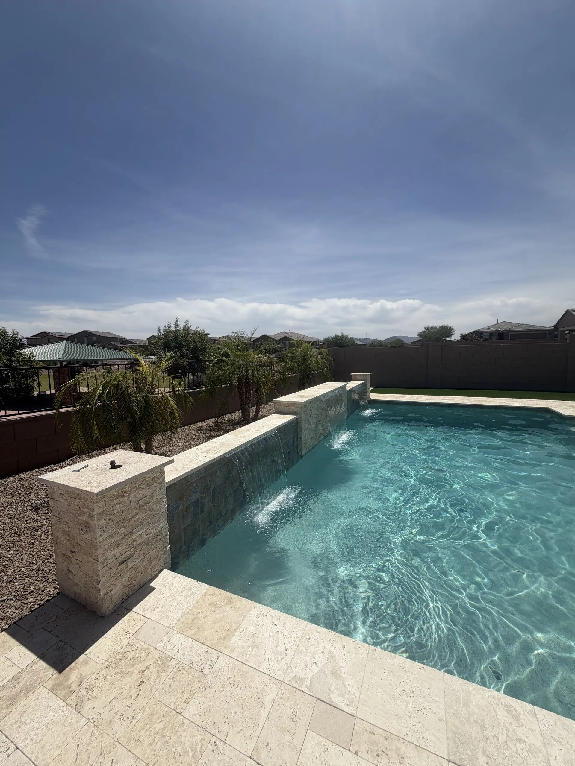 Raised tile wall with sheer descents and stacked stone pillar along a travertine pool deck
