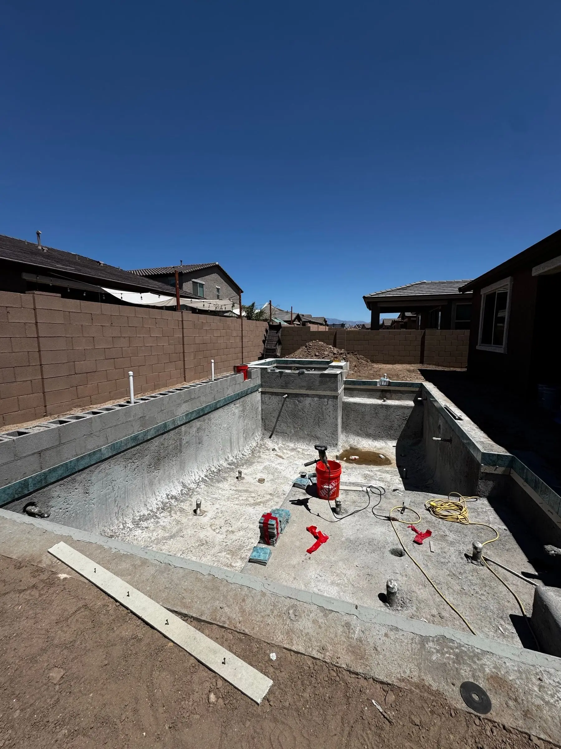 Completed shotcrete shell of a rectangular pool with a raised spa at the far end.