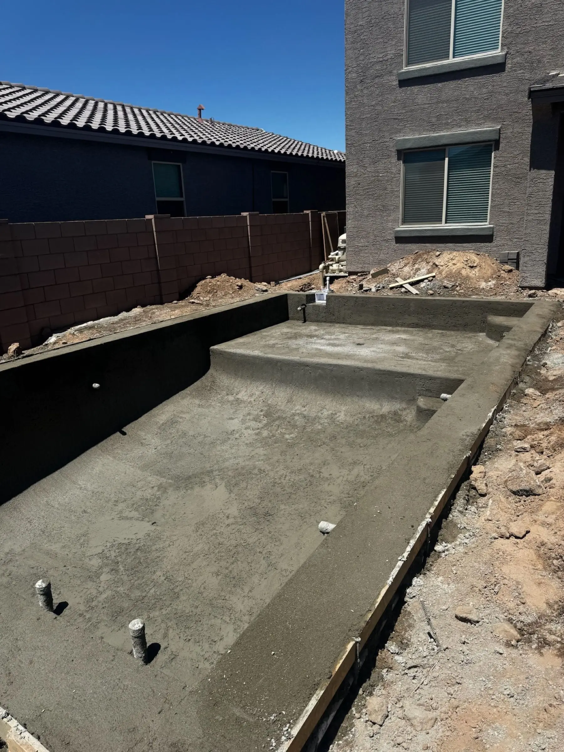 Fresh shotcrete shell of a rectangular pool with a built-in tanning ledge and steps, Marana, AZ.